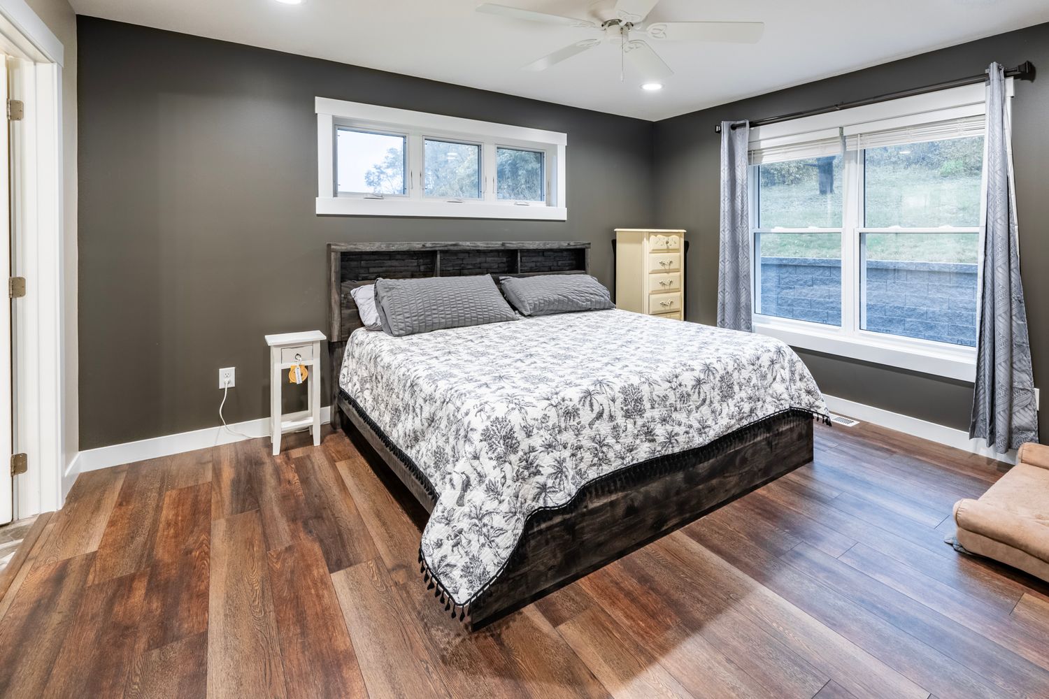 Master bedroom with dark accent walls, hardwood floors, and large windows providing natural light.