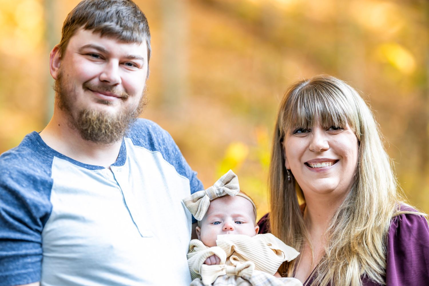 A family portrait taken outdoors with warm autumn colors in the background.