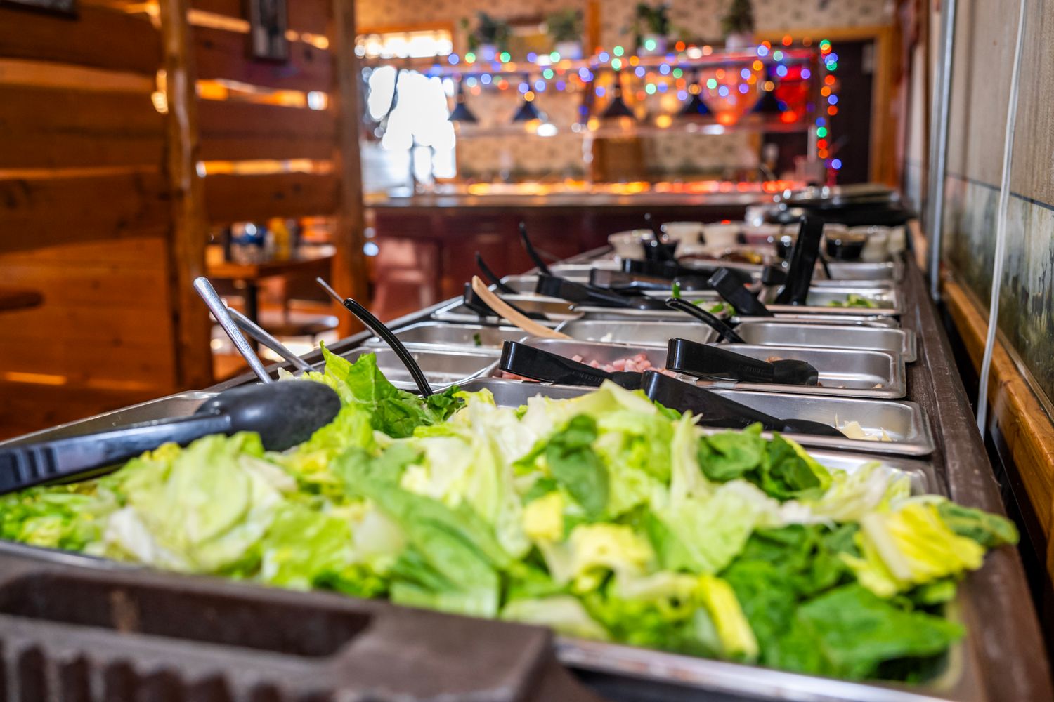 Fresh salad bar setup with lettuce and toppings in metal serving containers.