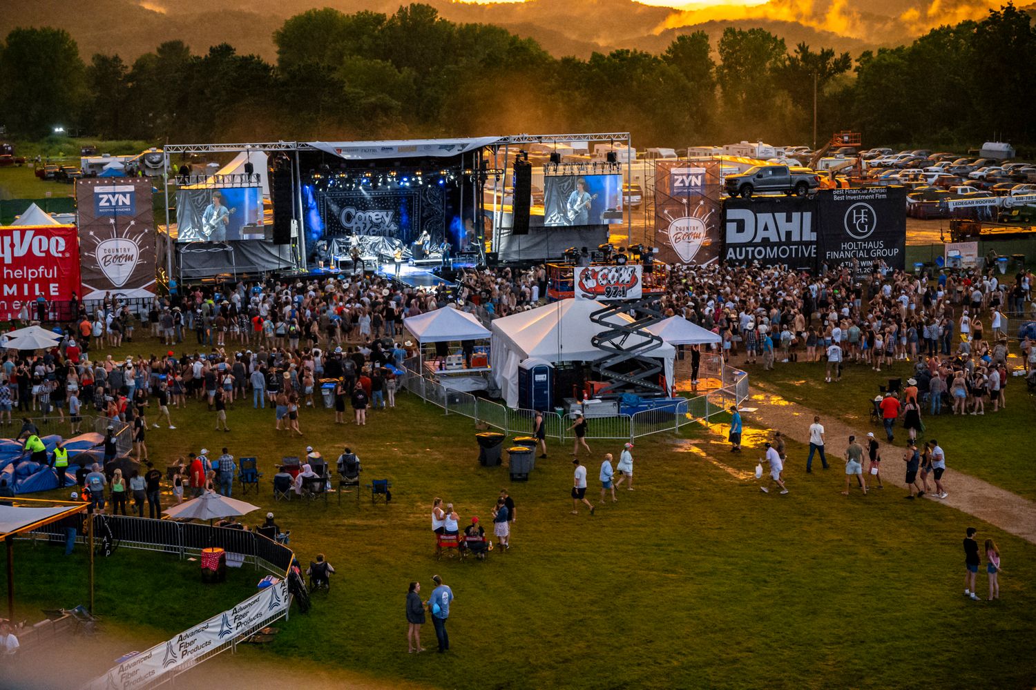 Panoramic view of a festival grounds at sunset with vendor tents and large crowds.