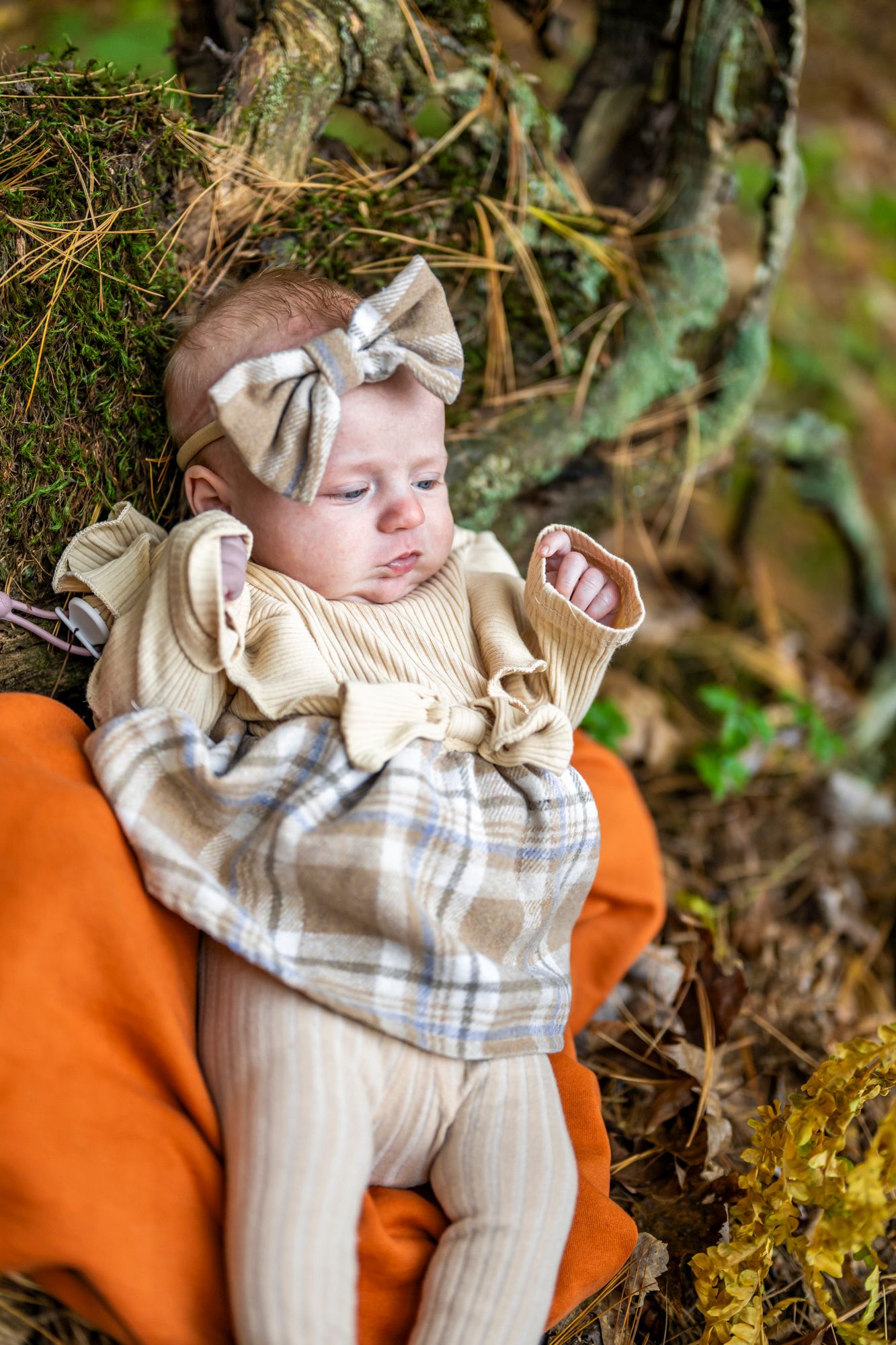 Baby wearing beige outfit lying on orange blanket during outdoor autumn photoshoot.