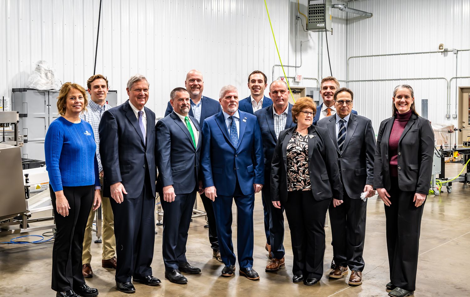 Group photo of business professionals lined up in formal attire with American flags in the background.