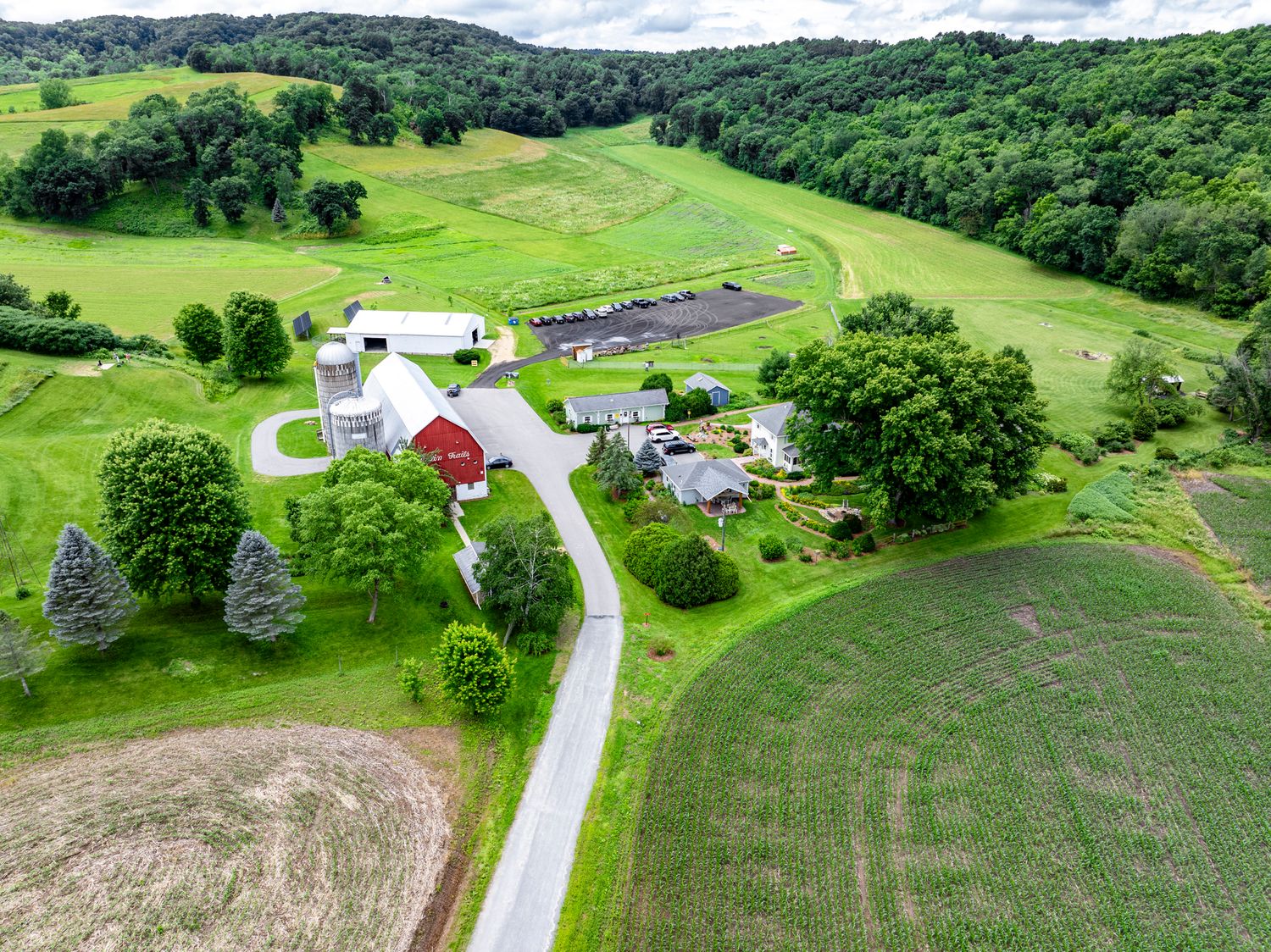 Drone view of a sprawling countryside farm property with barns and winding roads through green fields.