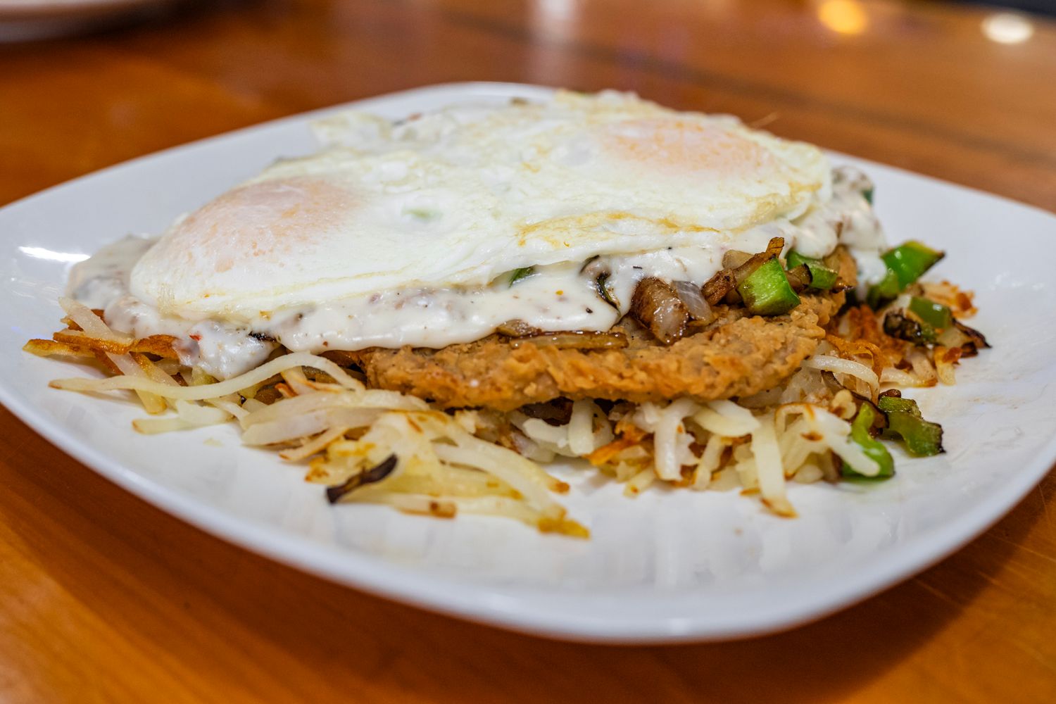 Breakfast hash topped with eggs and melted cheese on a white plate.