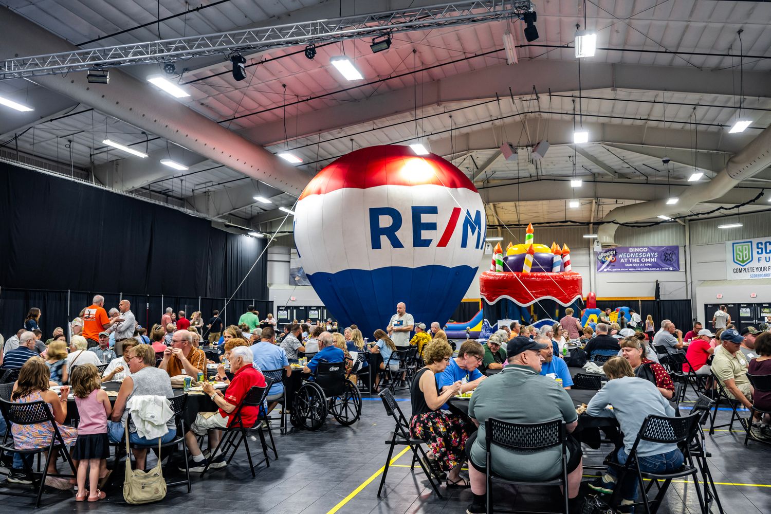 Panoramic view of a spacious venue with RE/MAX branding and groups seated at round tables.
