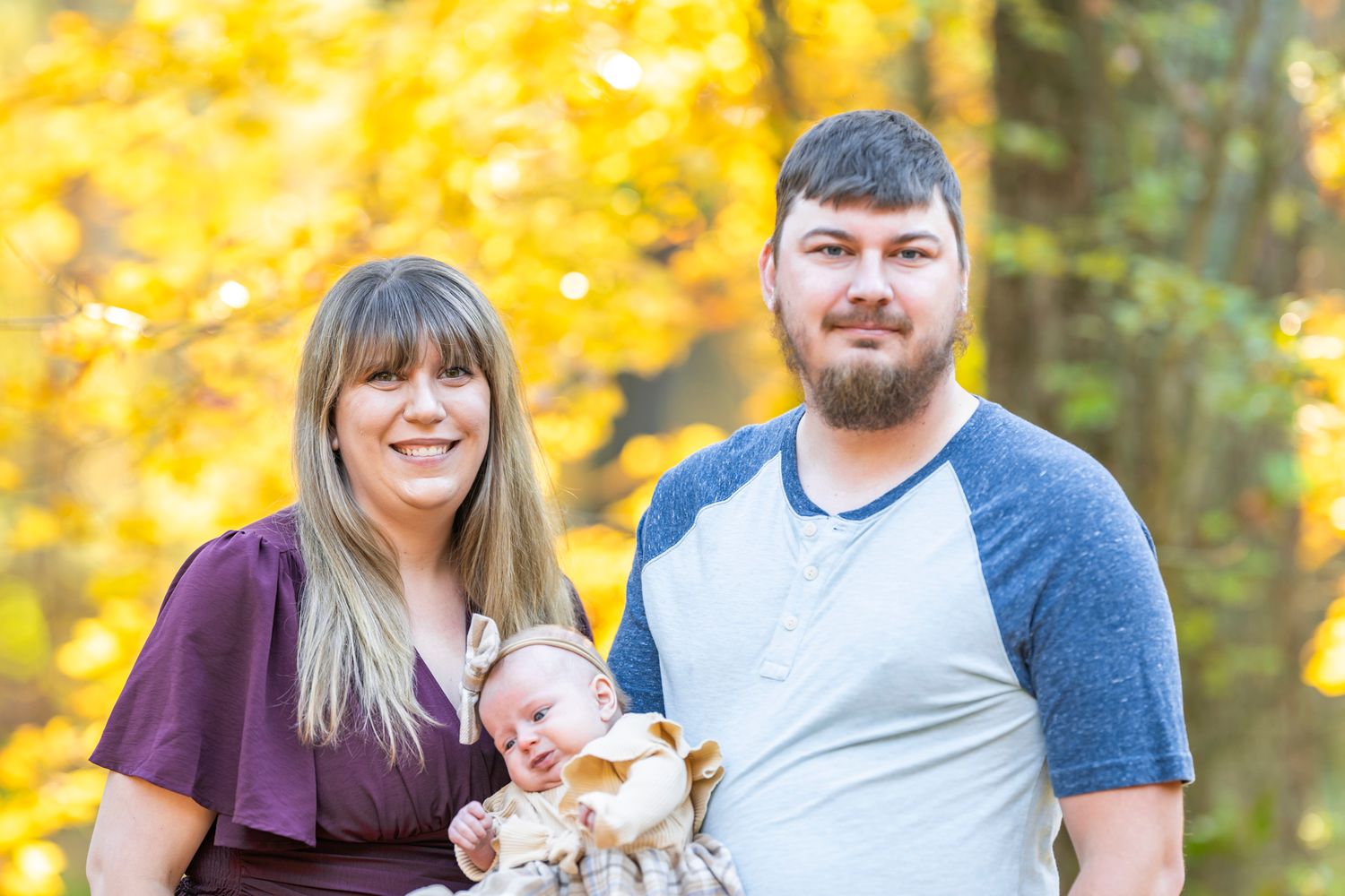 A family poses together during autumn with golden foliage in the background.