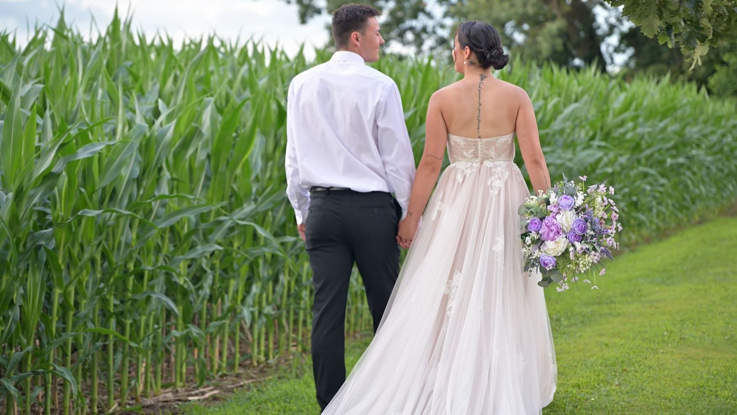 Couple walking through a lush green garden path during an outdoor wedding ceremony.