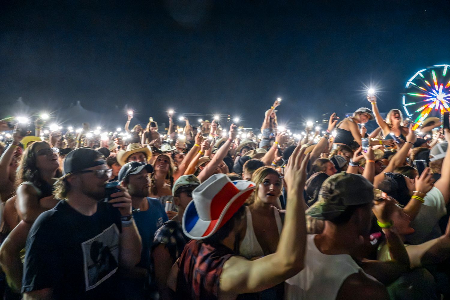 Concert crowd holding up illuminated phones and lights during a nighttime performance.
