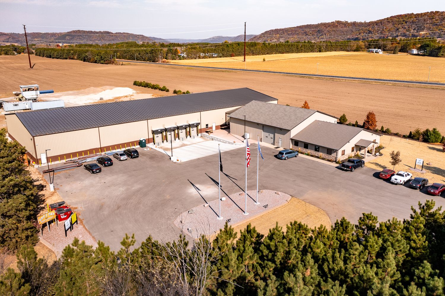 Drone shot of an industrial complex with multiple buildings and parking areas in a rural setting.