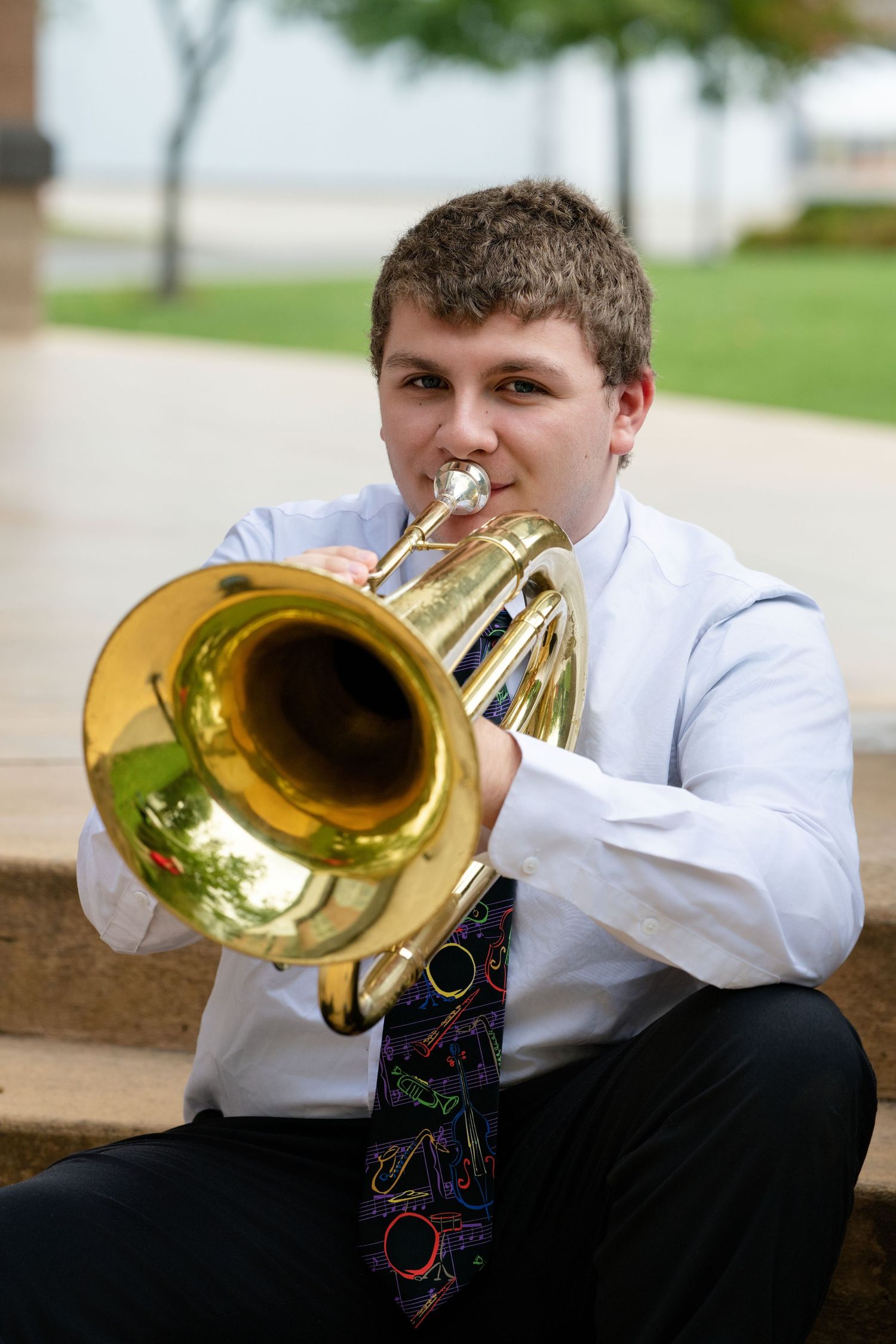 Musician plays shiny brass trumpet while wearing formal white shirt.