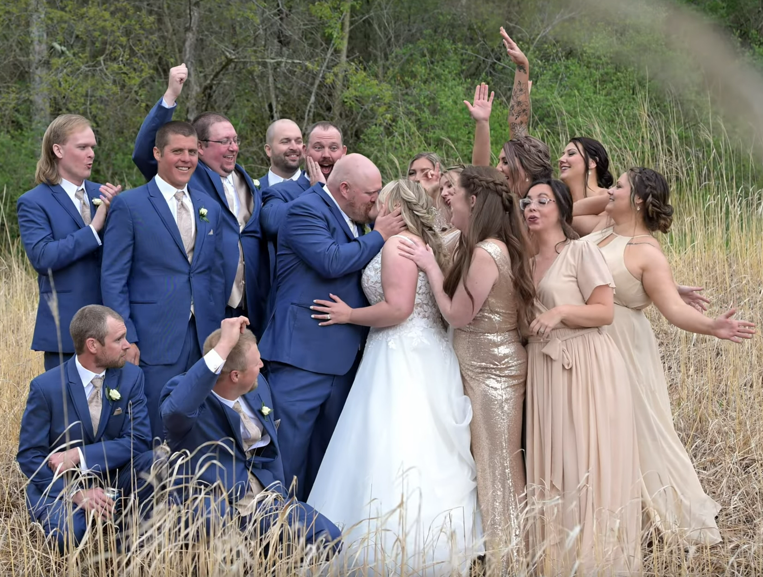 Wedding party poses for outdoor group photos in blue suits and beige dresses.