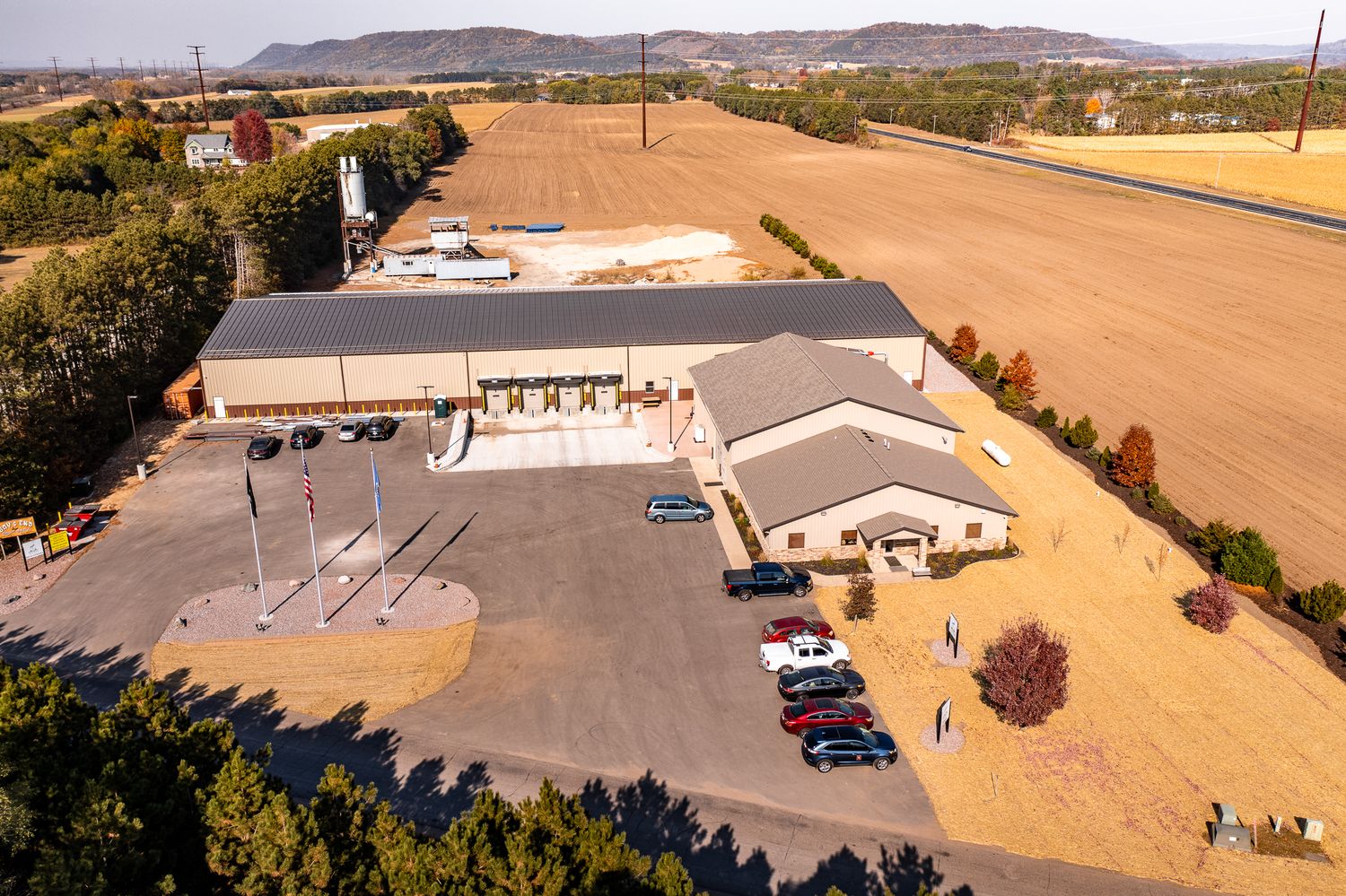 Aerial view of a commercial facility with loading docks and parking area surrounded by farmland.