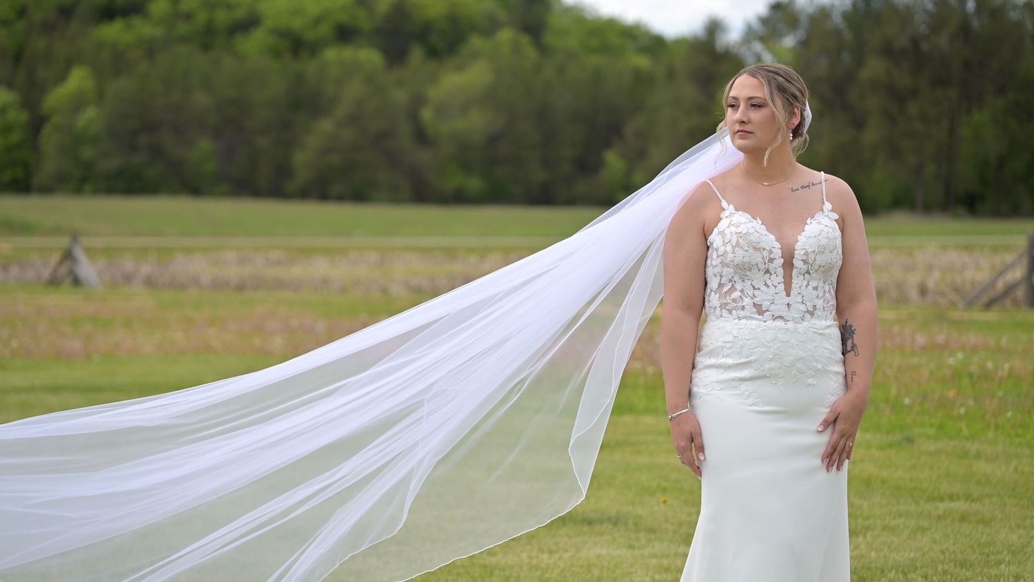A flowing white wedding dress veil trails across a grassy field during an outdoor photoshoot.