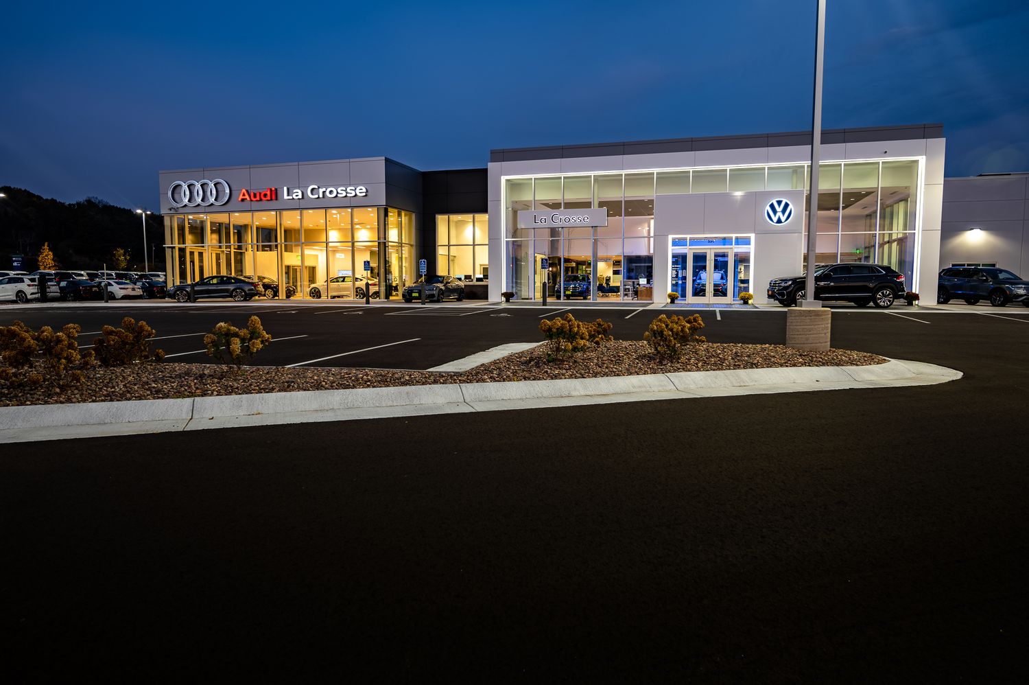 Two adjacent car dealerships with illuminated storefronts and showrooms at dusk.