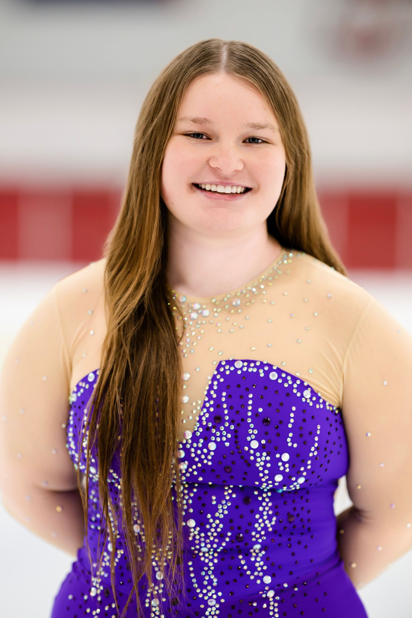 Figure skater poses in a bedazzled purple costume with rhinestone details.