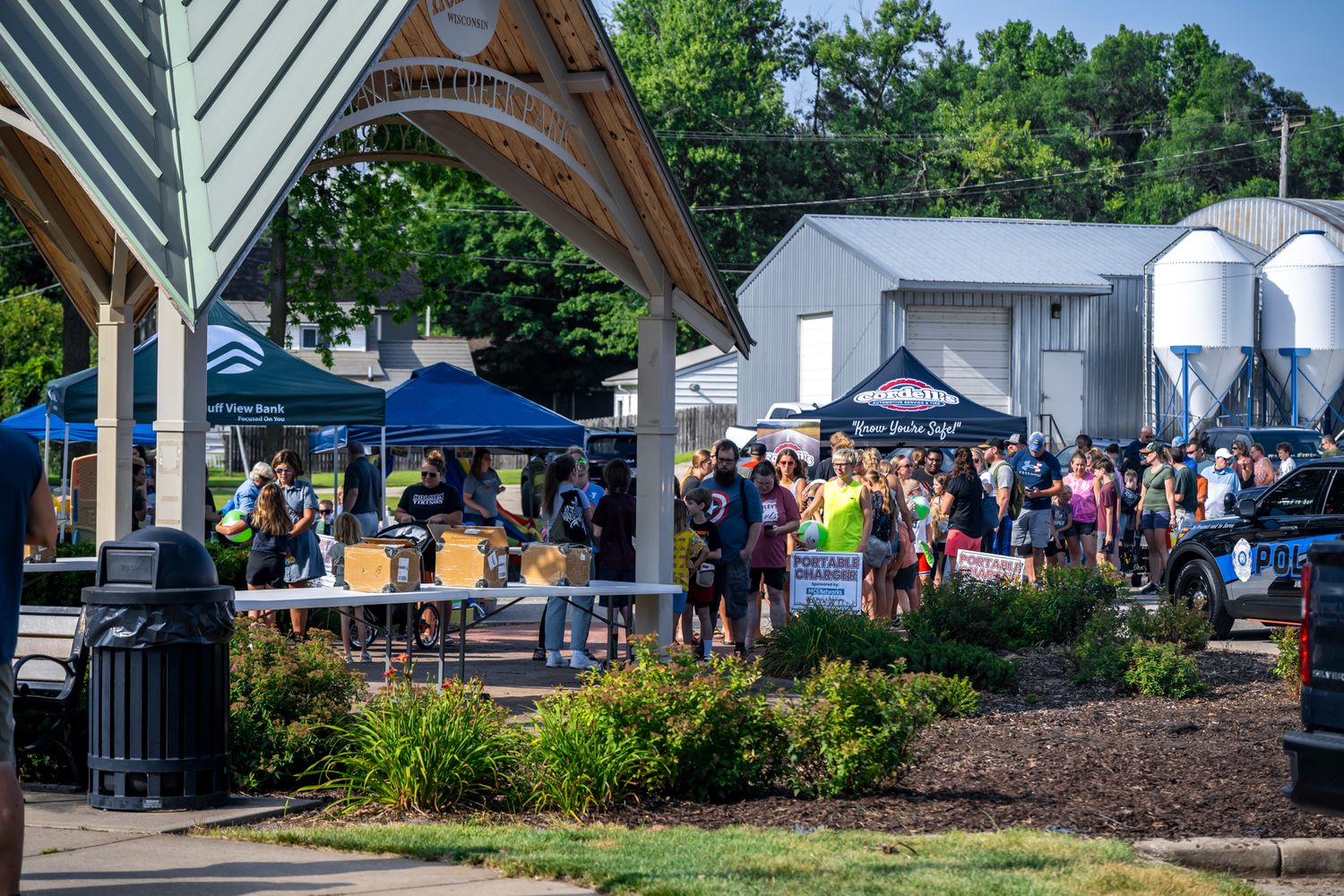 Outdoor pavilion with sponsor banners and tents set up for a community gathering.