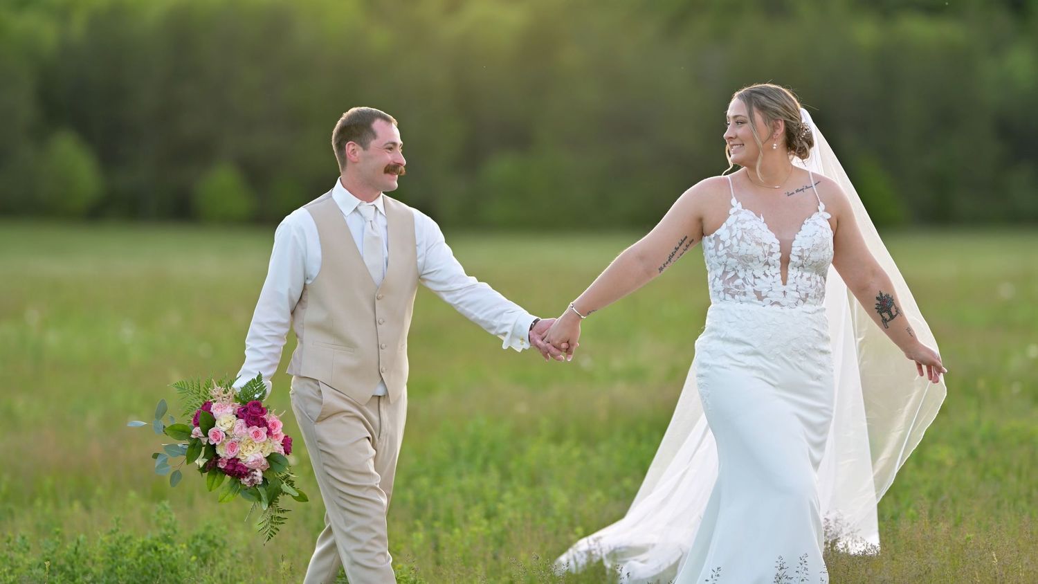Wedding couple walking hand in hand through a sunny green meadow.