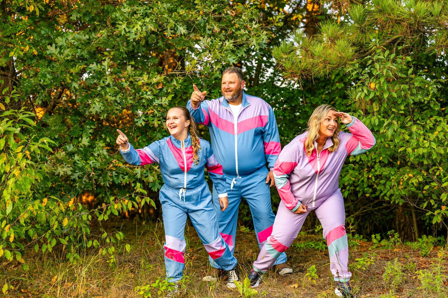 Three people wearing retro-style tracksuits posing playfully in an apple orchard.