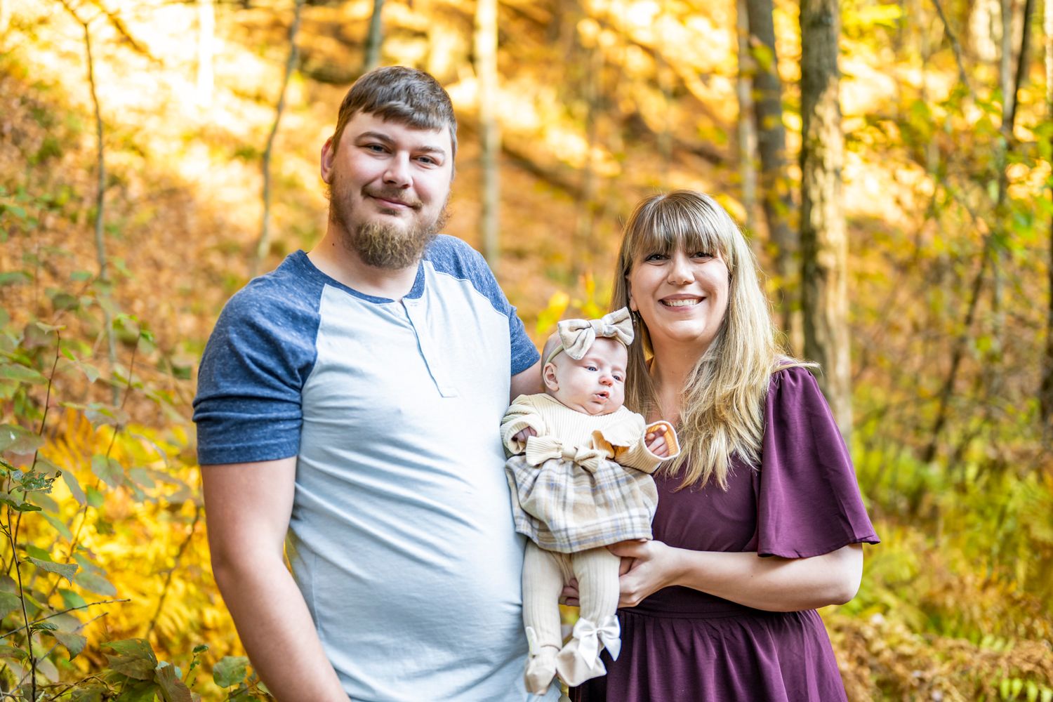 Family photo session captured in golden hour sunlight with autumn trees in background.