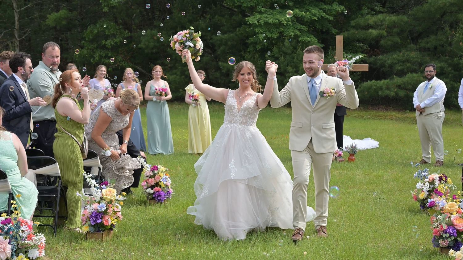 Wedding party and guests celebrating on grassy lawn with colorful floral arrangements.