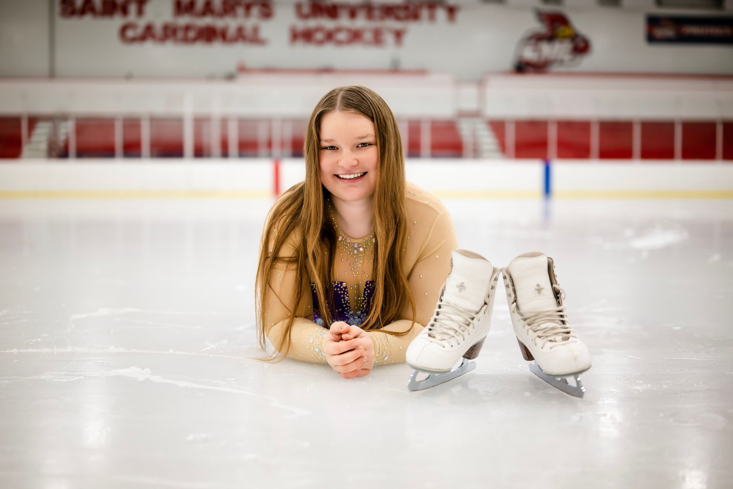 Ice skater poses on a hockey rink with white figure skates.