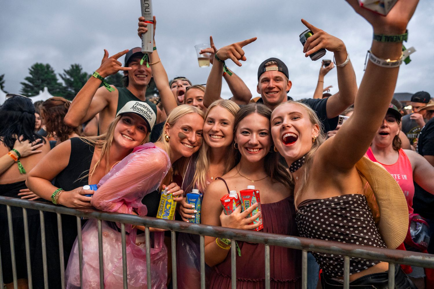 Excited festival attendees celebrate at concert barrier with drinks raised in the air.