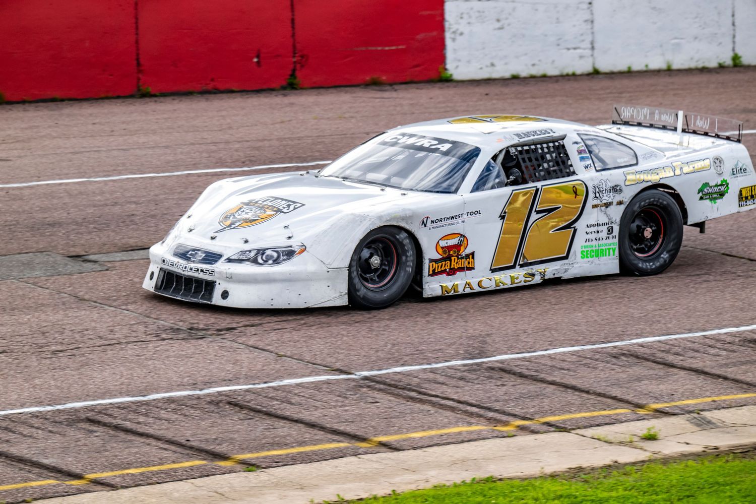 White and red stock cars racing on an asphalt track during a competitive event.
