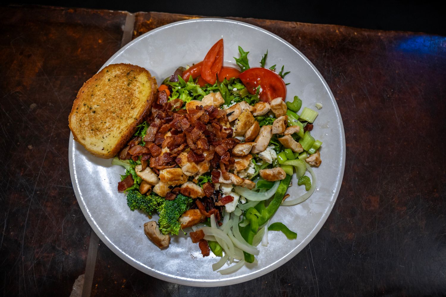 Fresh garden salad topped with grilled chicken, nuts and a slice of toasted bread on a white plate.