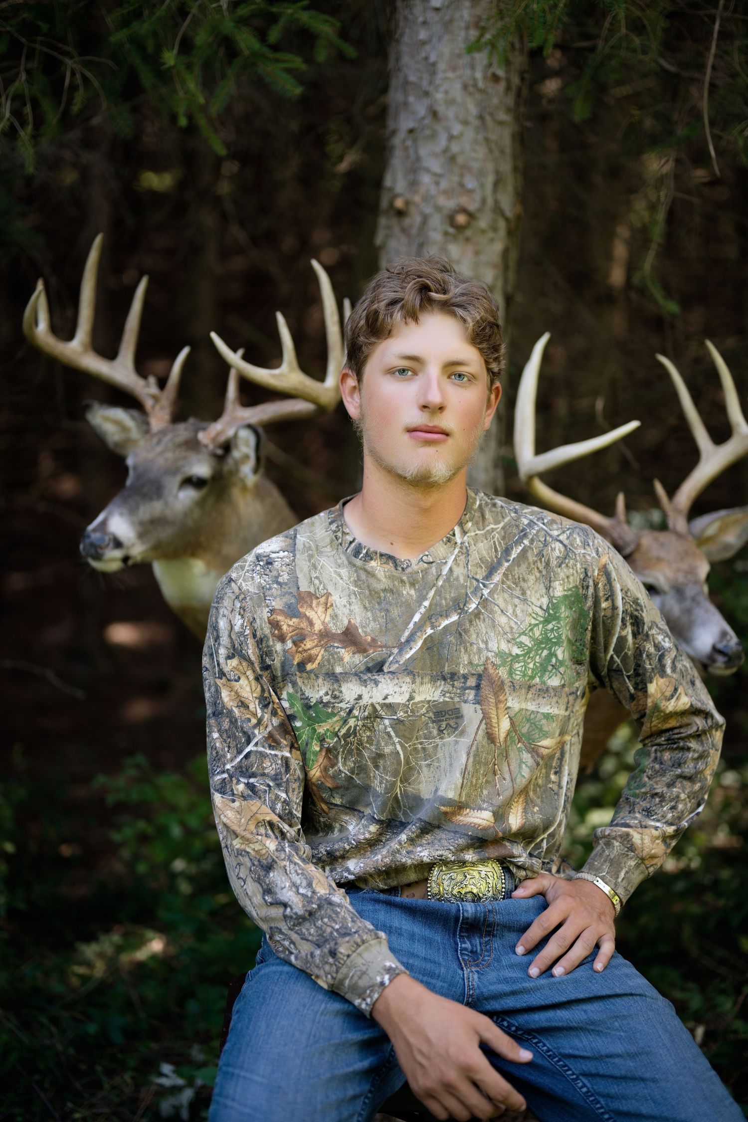 Outdoor portrait session with camouflage clothing and deer antlers in background.