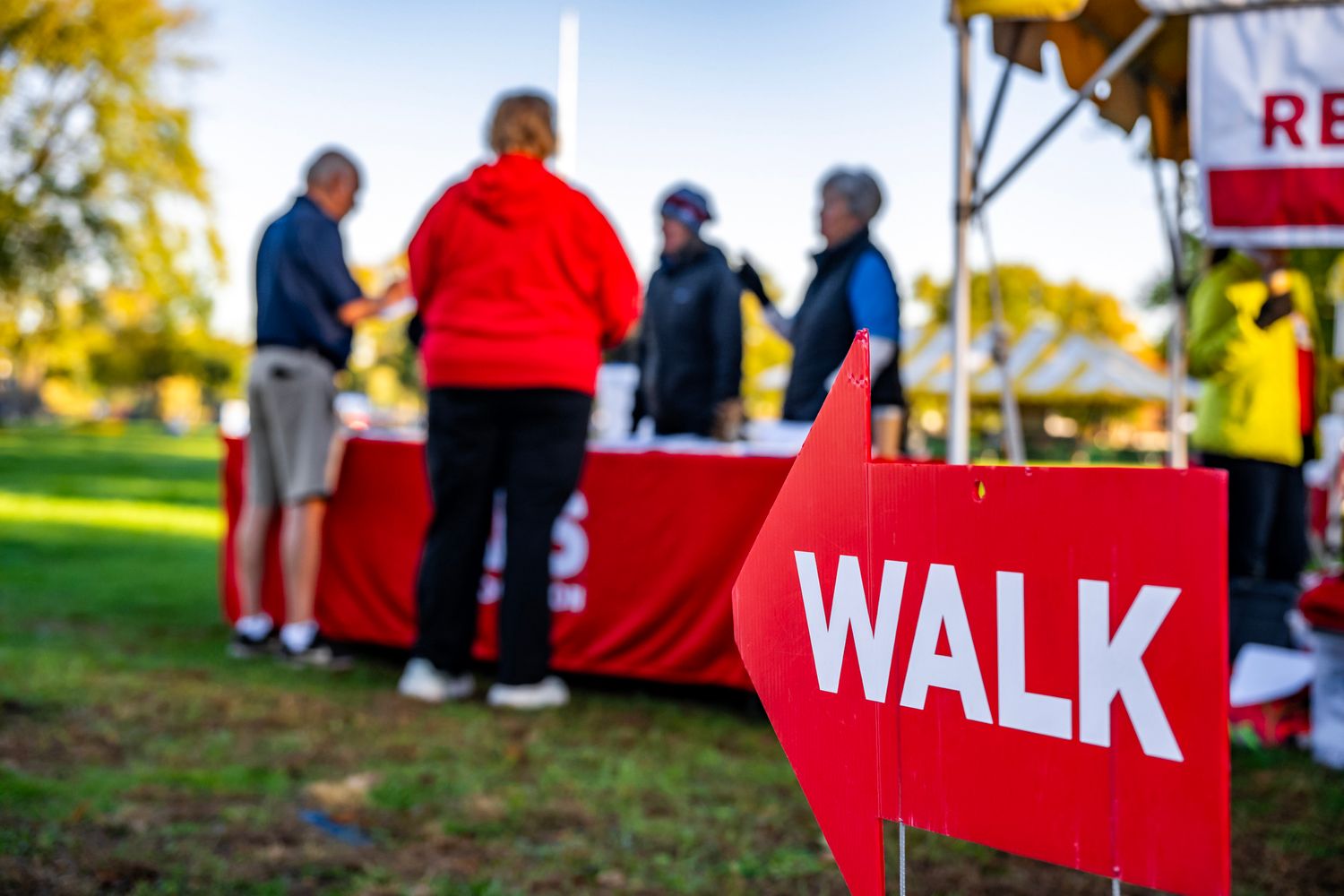 Red and white walk signs and banners at outdoor community event.