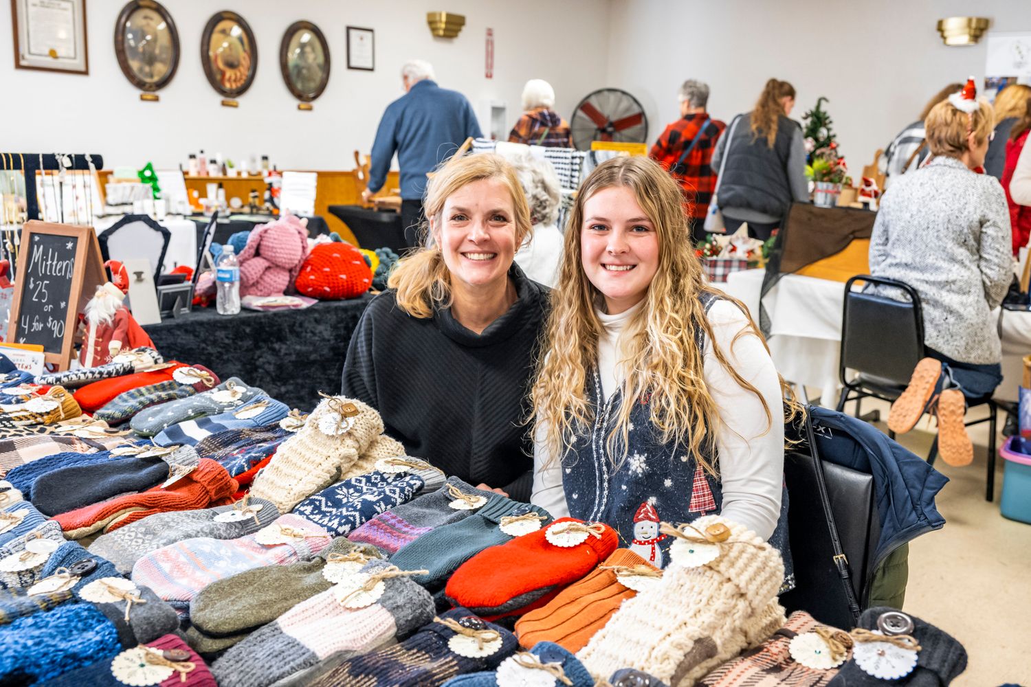 Holiday craft fair or market with vendors displaying merchandise at decorated tables.
