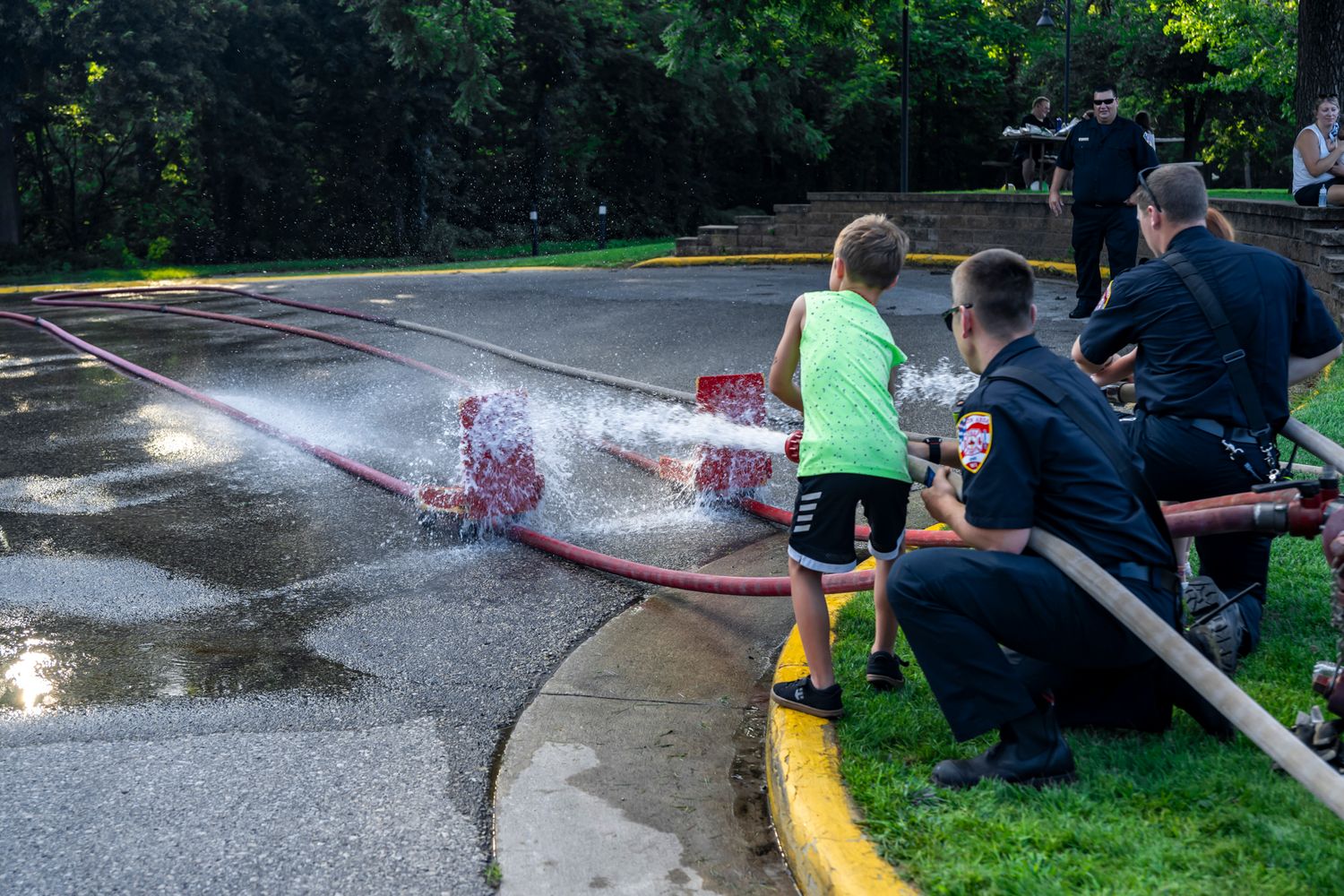 Children playing with water sprays from fire hoses at a community event.