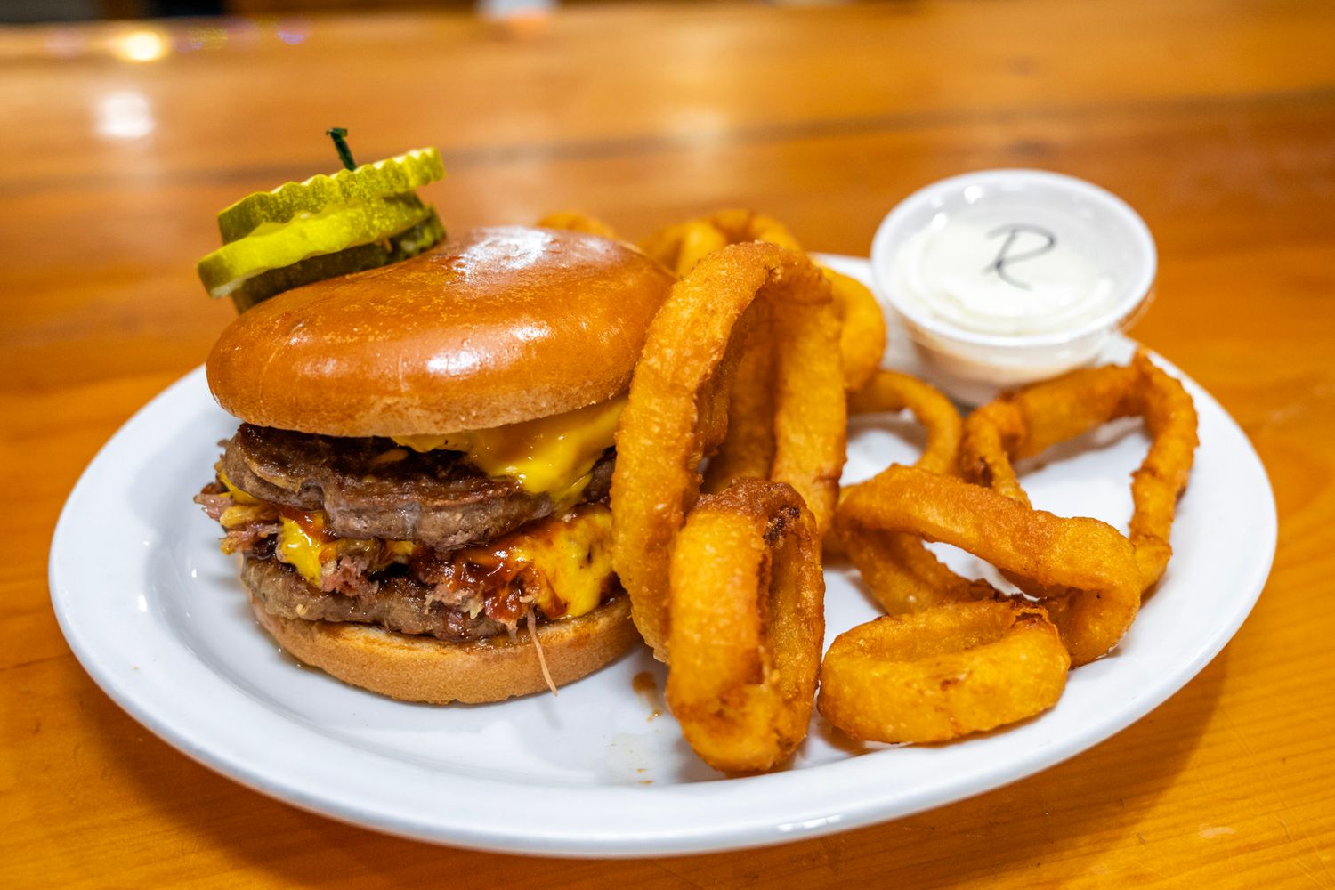 Juicy burger with onion rings and dipping sauce served on a white plate.