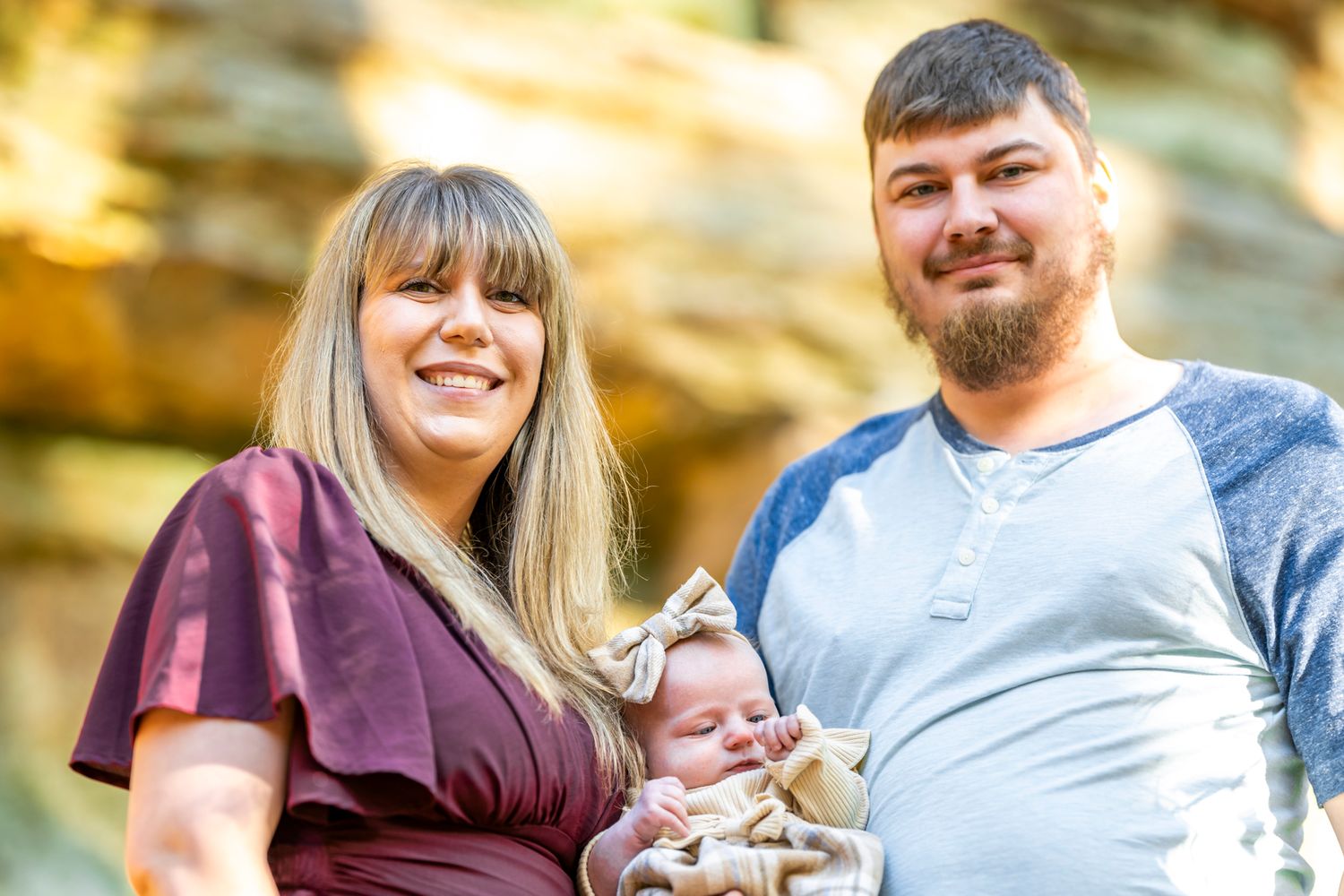 A couple with an infant photographed against a backdrop of golden fall foliage.