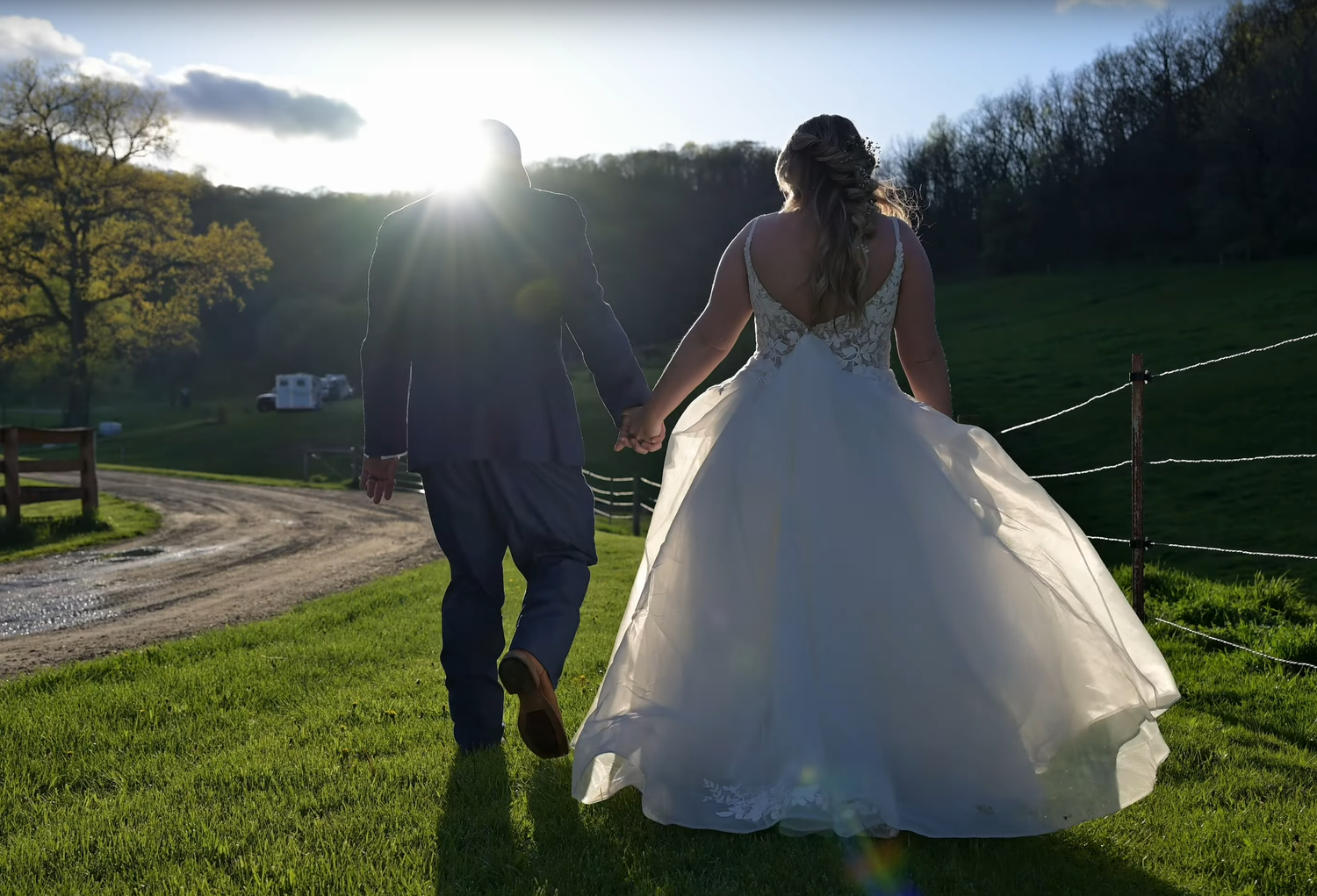 Newlyweds walking hand in hand on a hillside path at sunset.