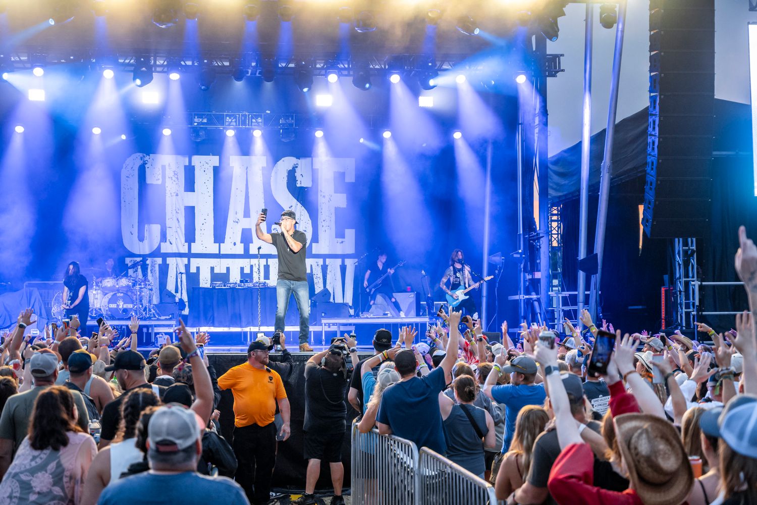 Wide shot of a concert venue with blue lighting and crowd visible in the foreground.