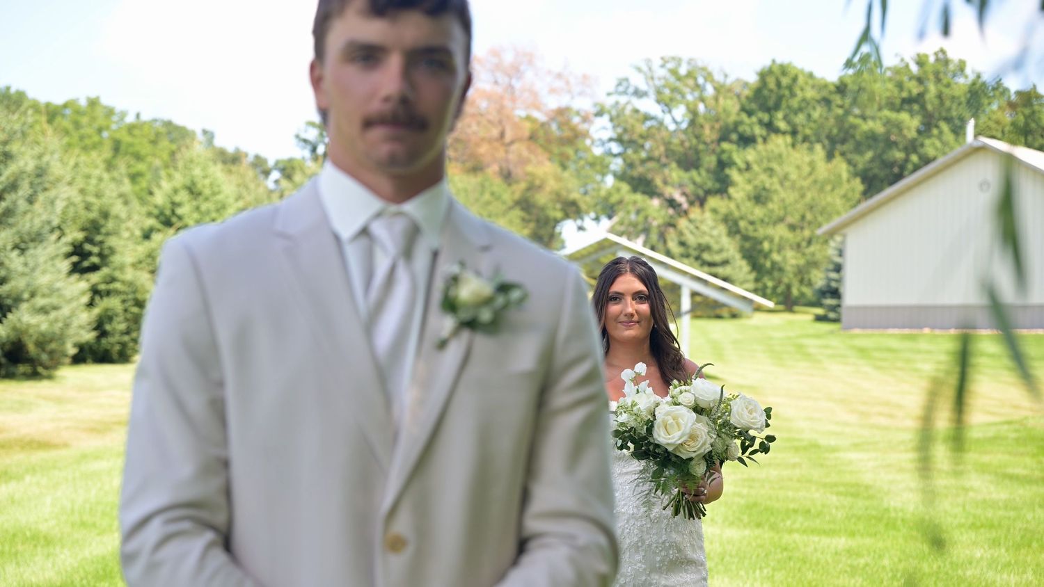Groomsmen in light gray suits with boutonnieres stand on green lawn.