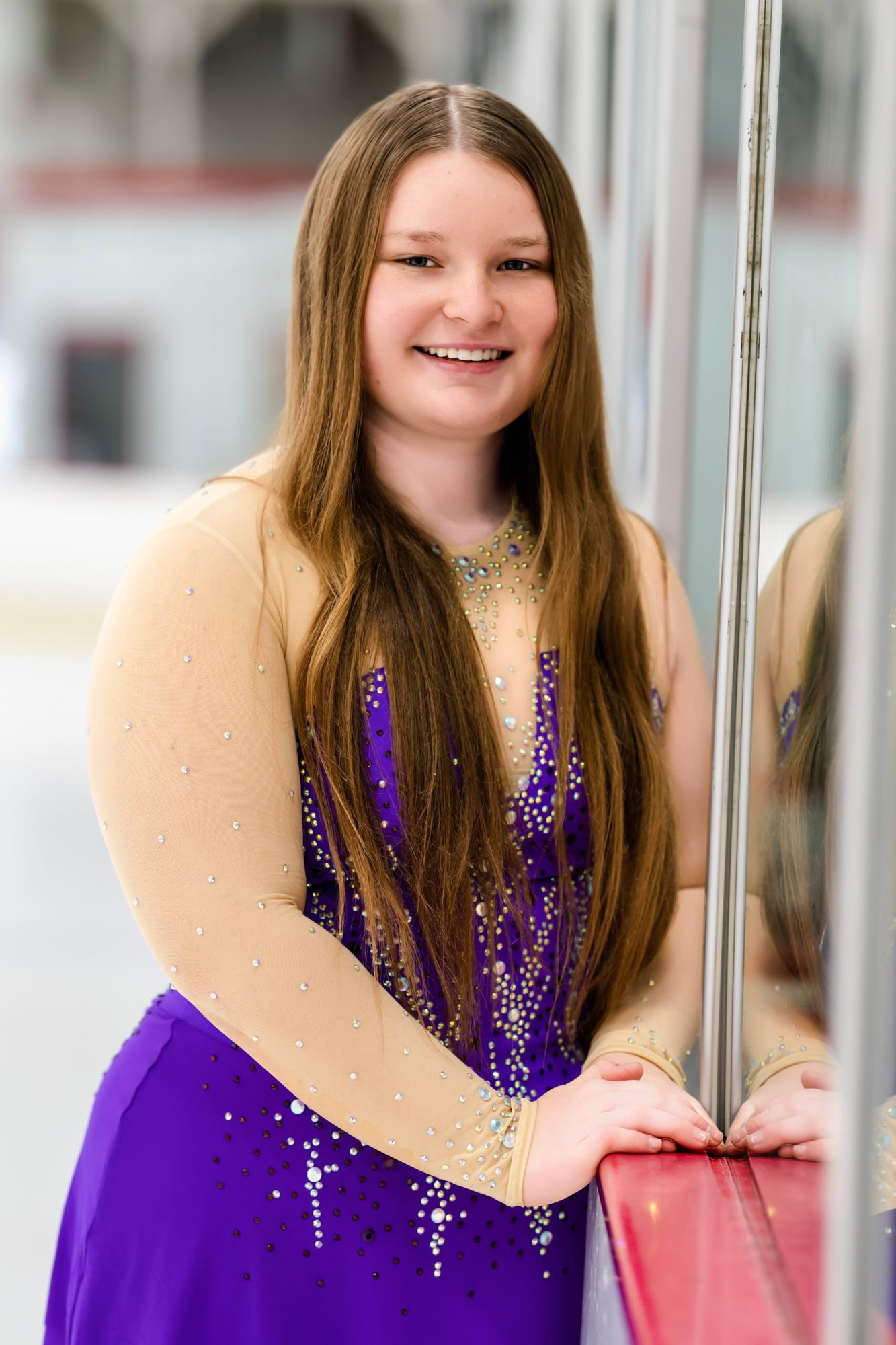 Figure skater in a sparkly purple dress poses gracefully on ice rink.
