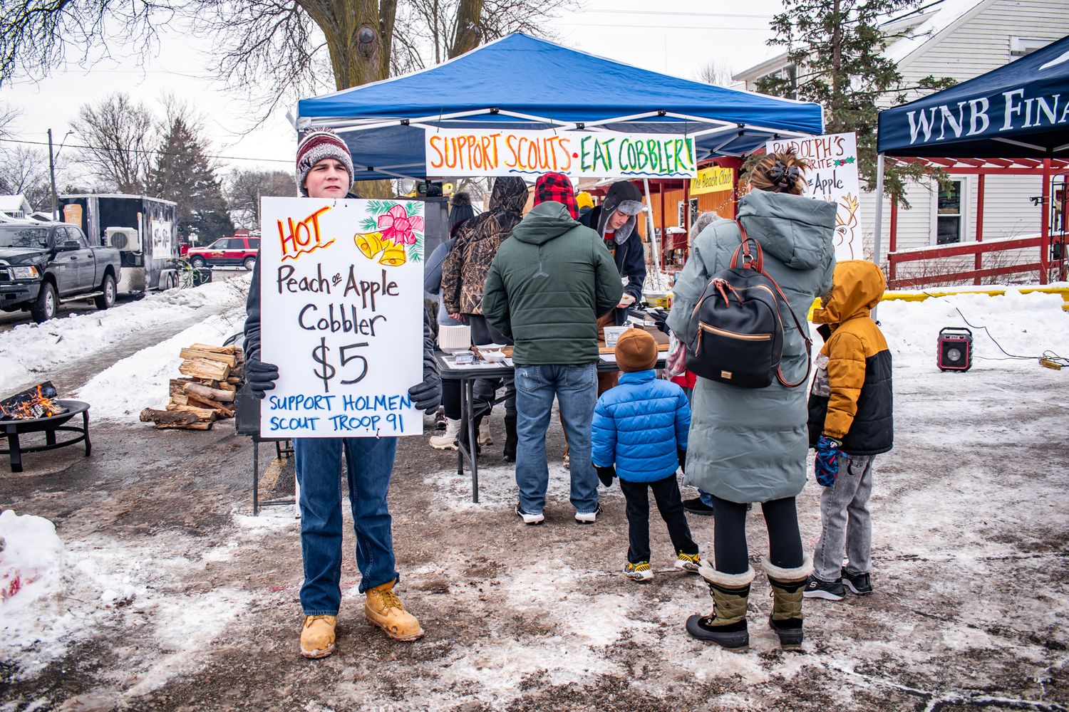 Winter market stalls with vendors and customers in snowy outdoor setting.
