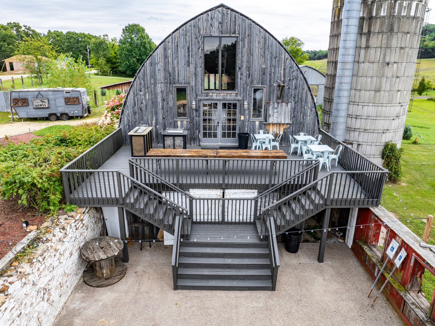 A rustic barn converted into a modern event space with a large deck and staircase next to a silo.
