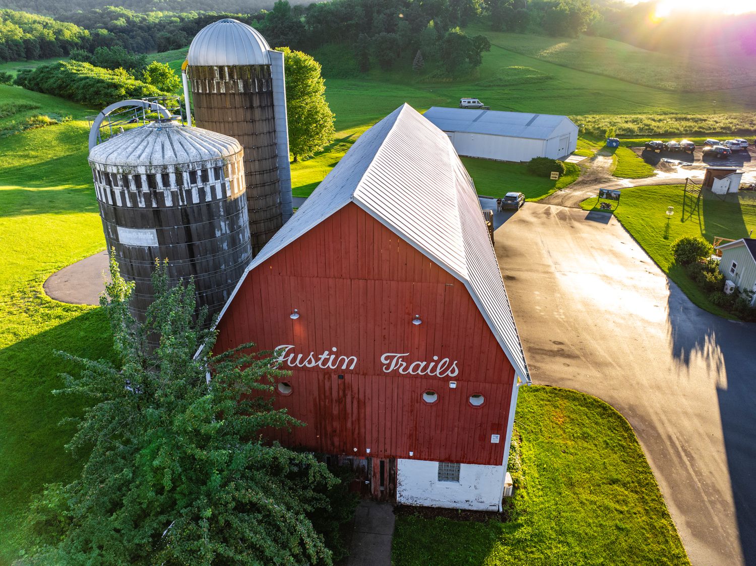 Aerial panorama of a scenic rural farm with red barns and rolling green hills at sunset.