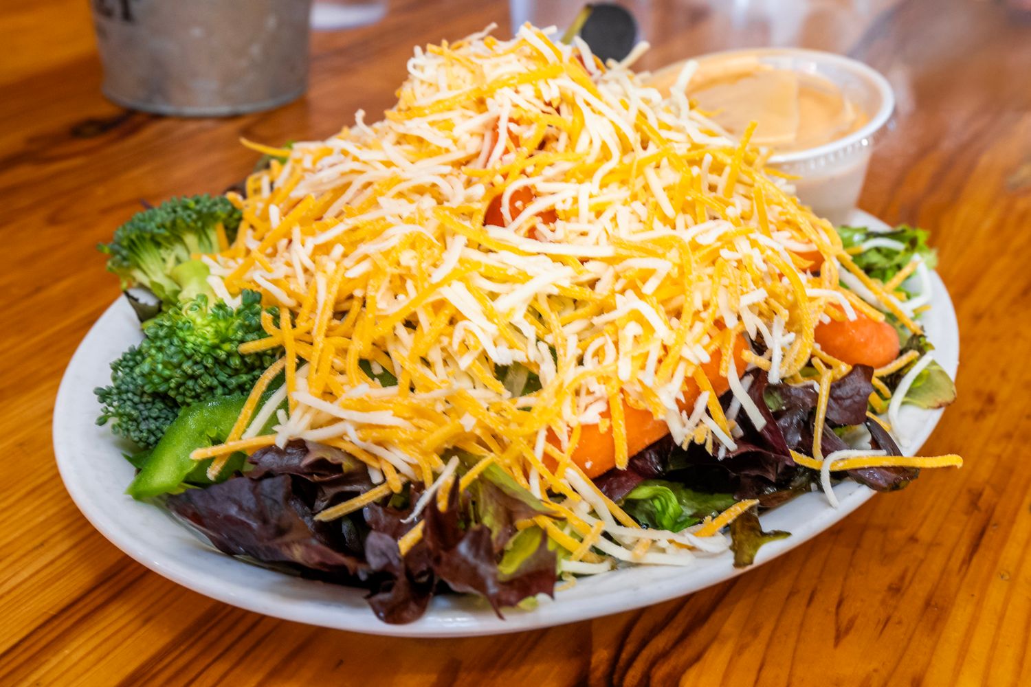 Fresh garden salad topped with shredded cheddar cheese and steamed broccoli on a white plate.