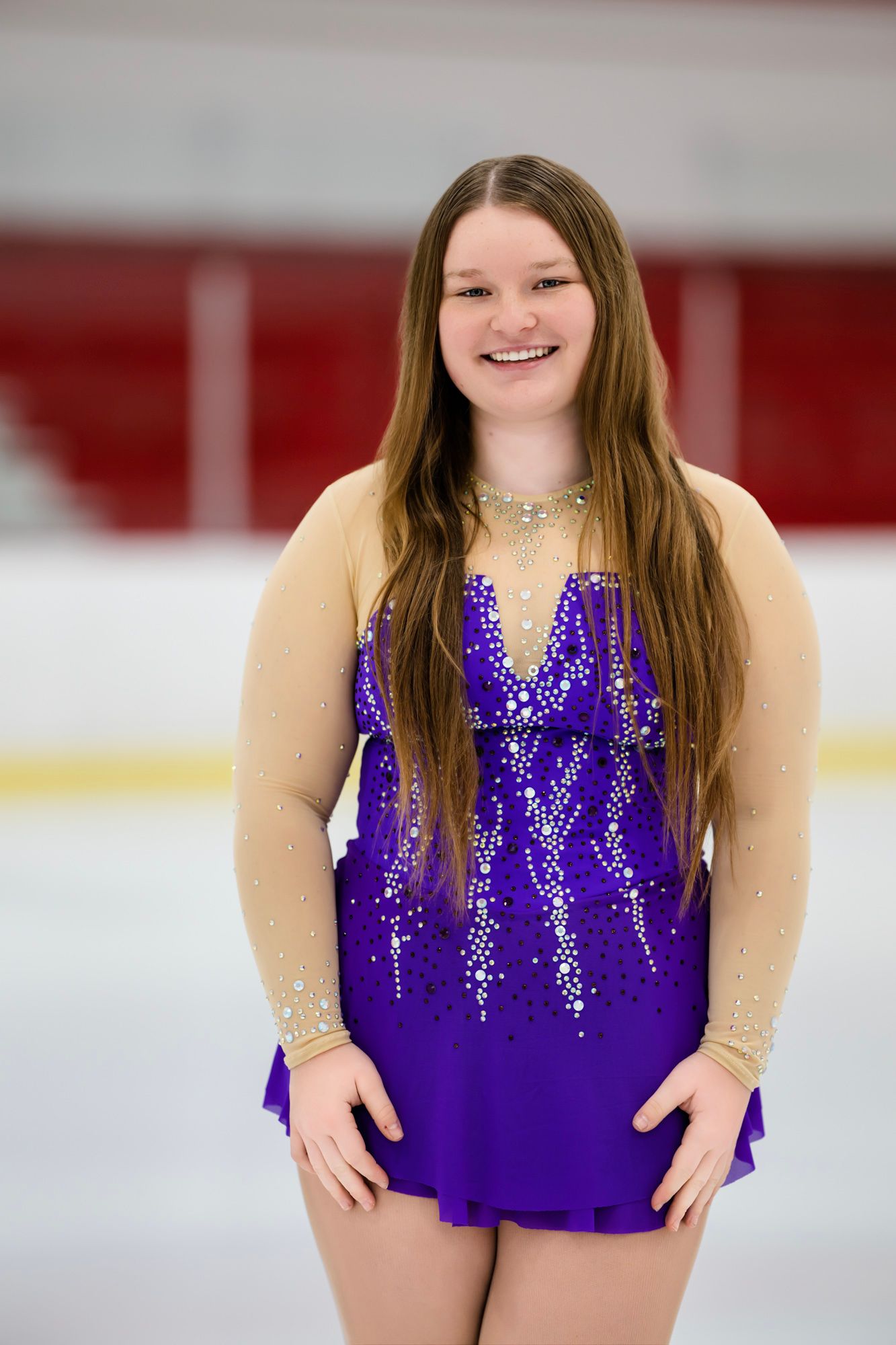 Ice skater wearing a vibrant purple performance dress with sequins stands on the rink.