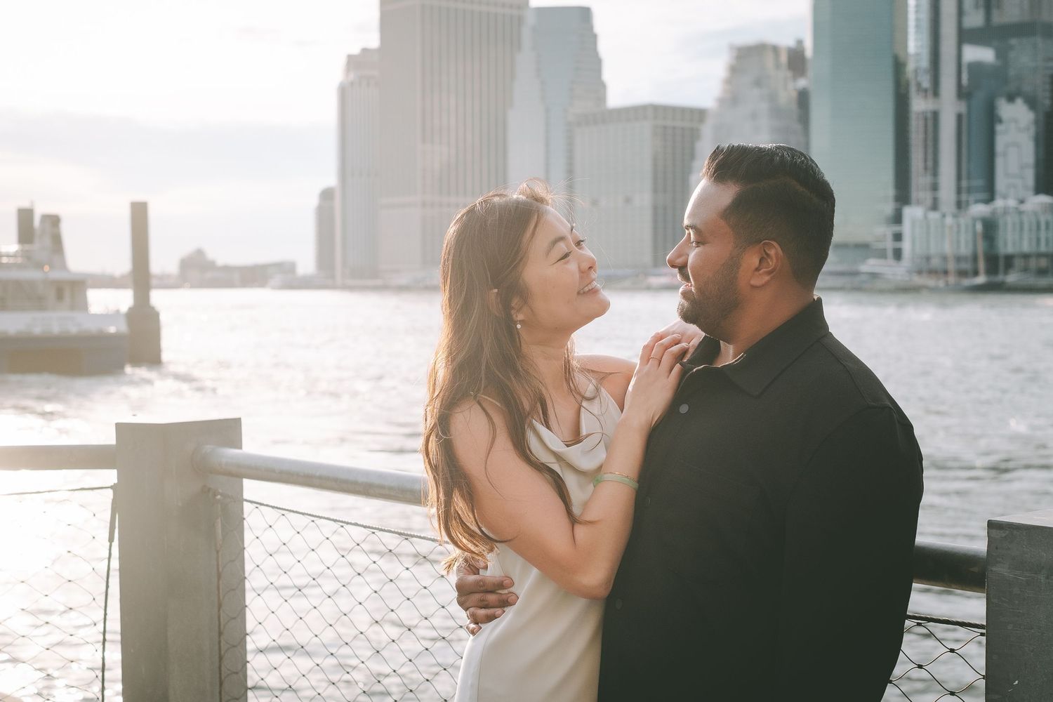 A couple posing together in the setting sun with a view of the Manhattan skyline