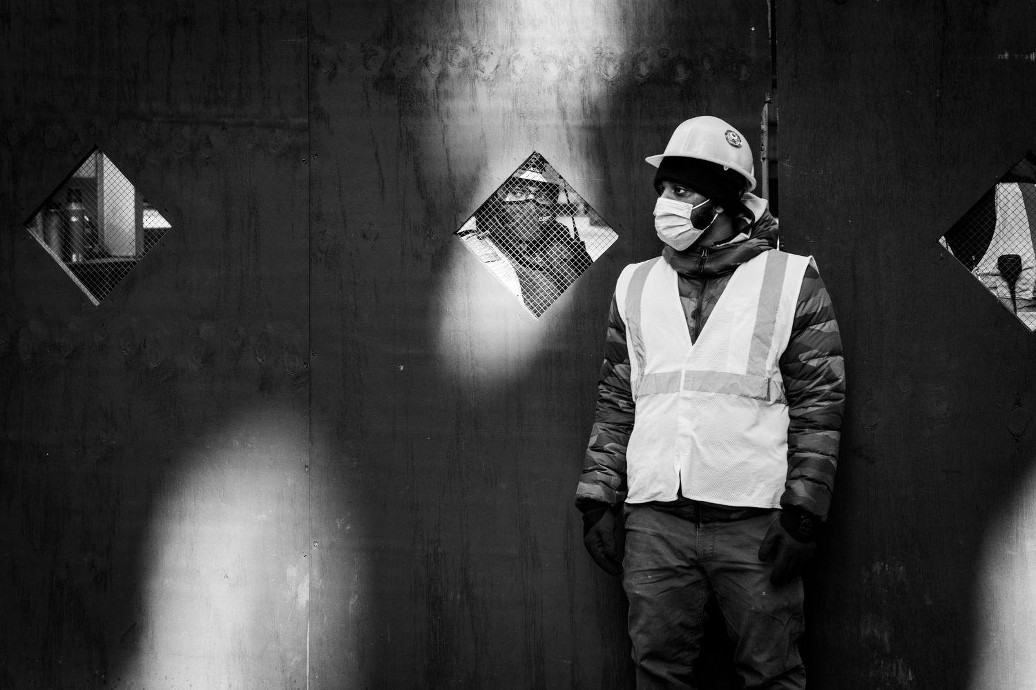 Two construction workers on either side of a wall, one looking through a cut-out in the wall