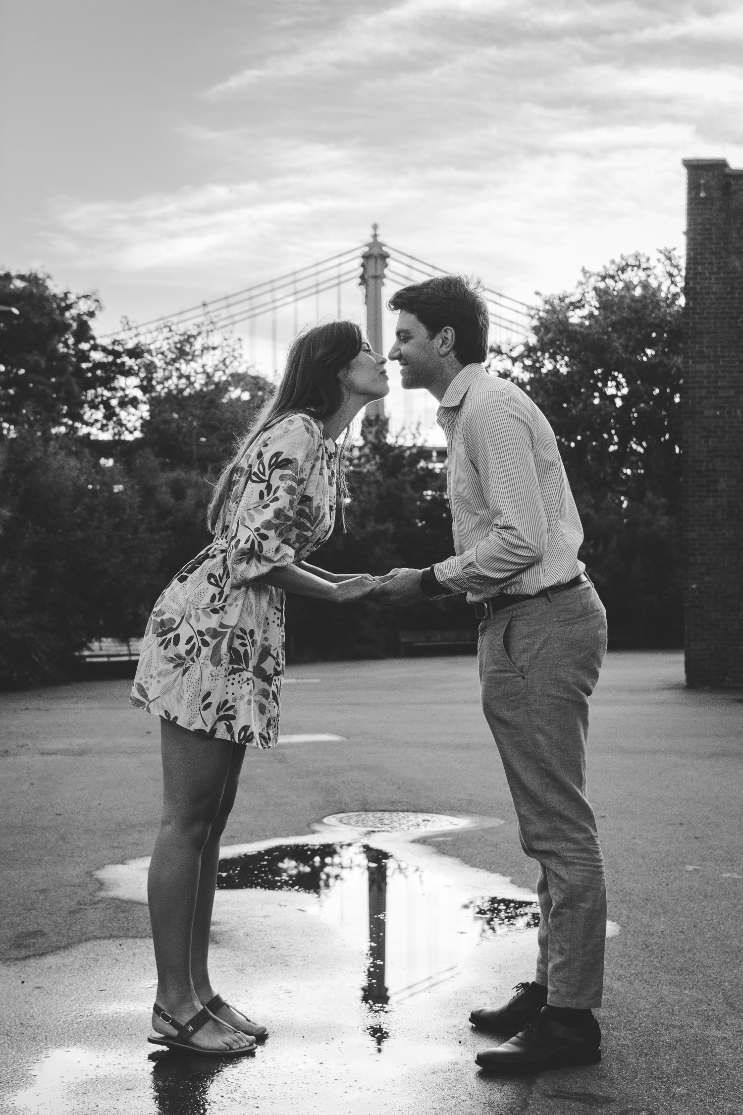 A couple kissing with the reflection of the Manhattan Bridge in a puddle beneath them