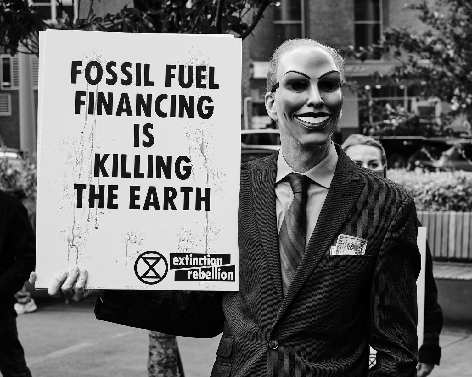 Masked individual holding a sign in protest of fossil fuels