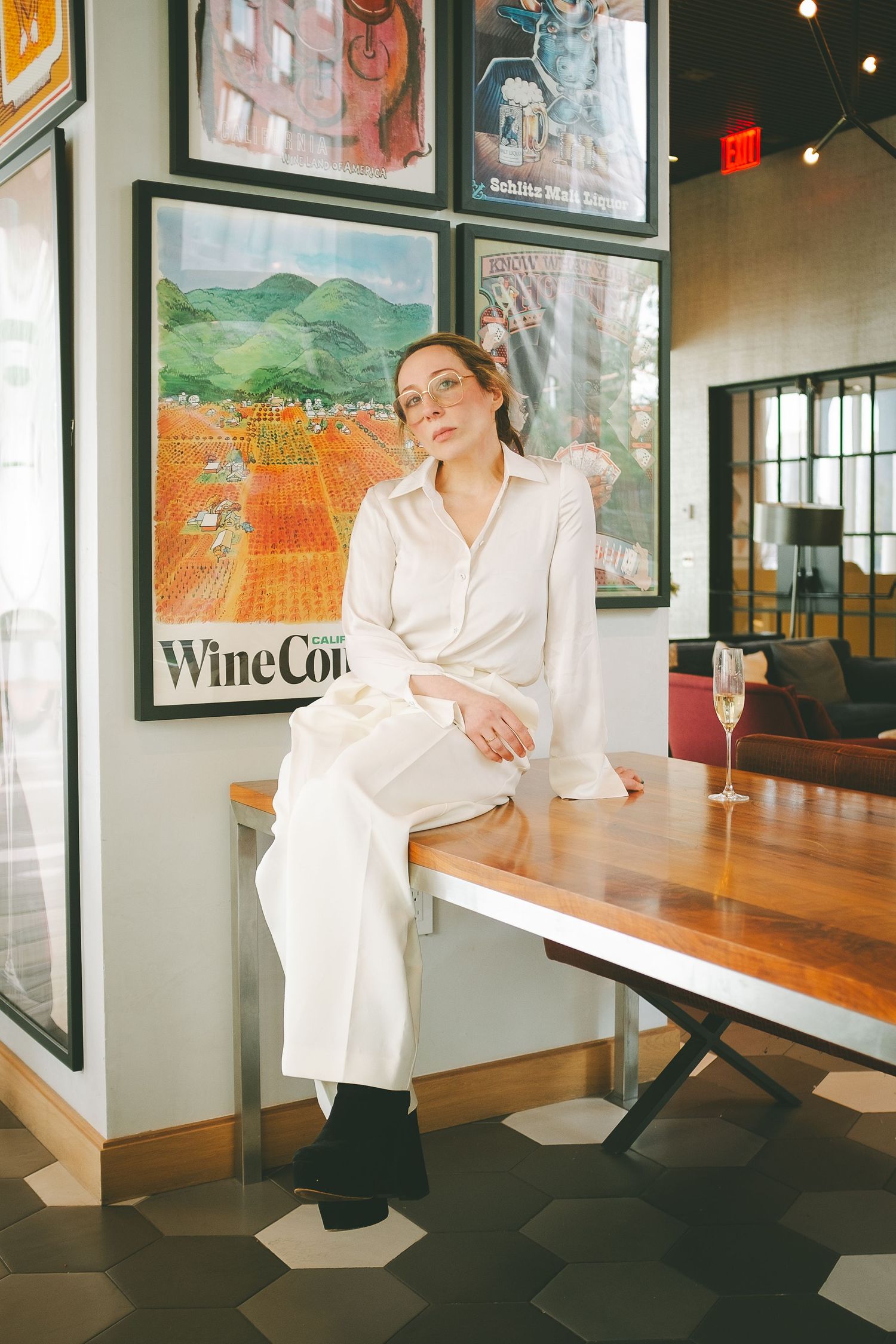 A woman dressed in white sitting on a table next to a glass of champagne
