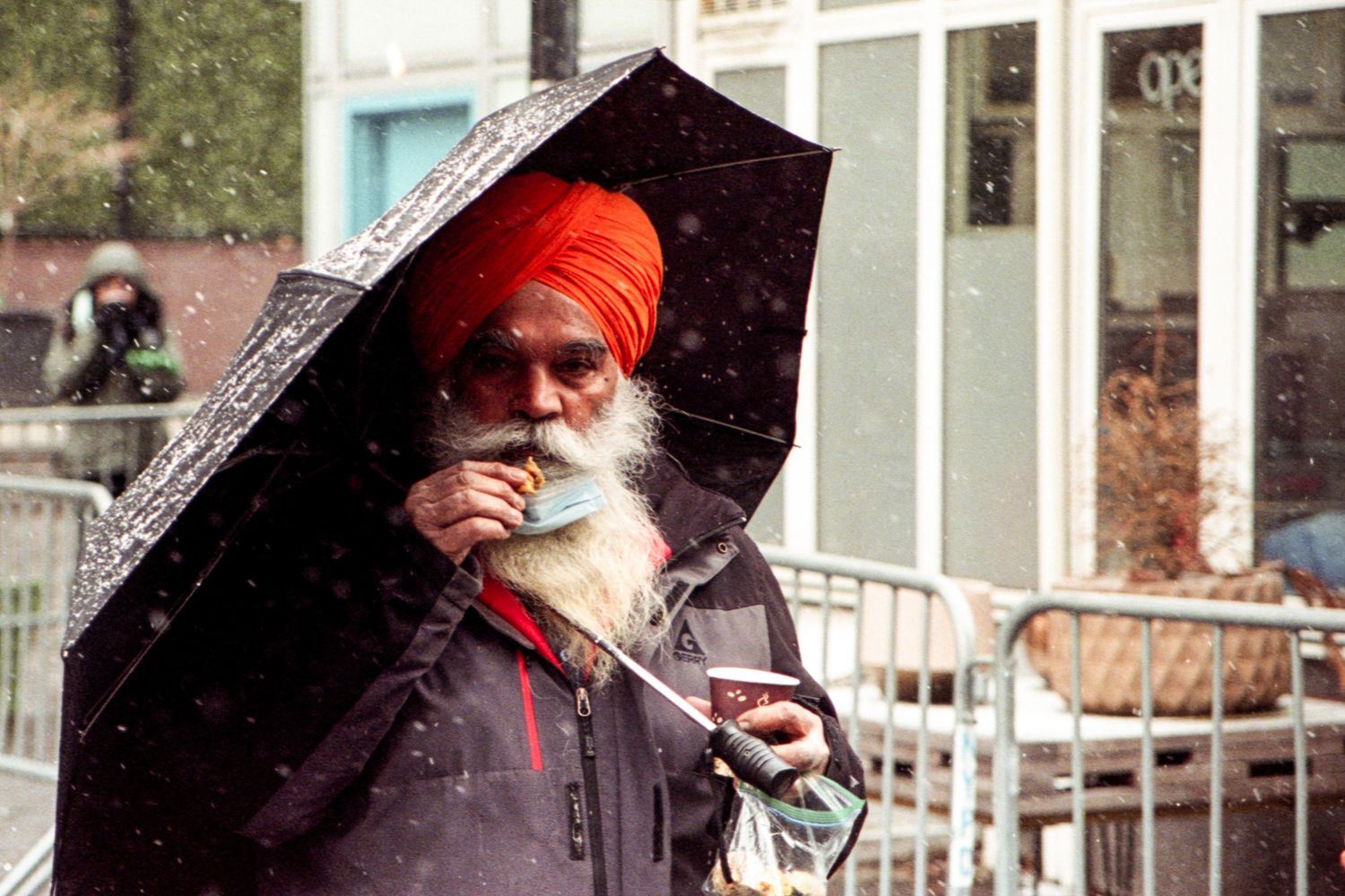 An Indian man eating a snack and holding an umbrella in the snow