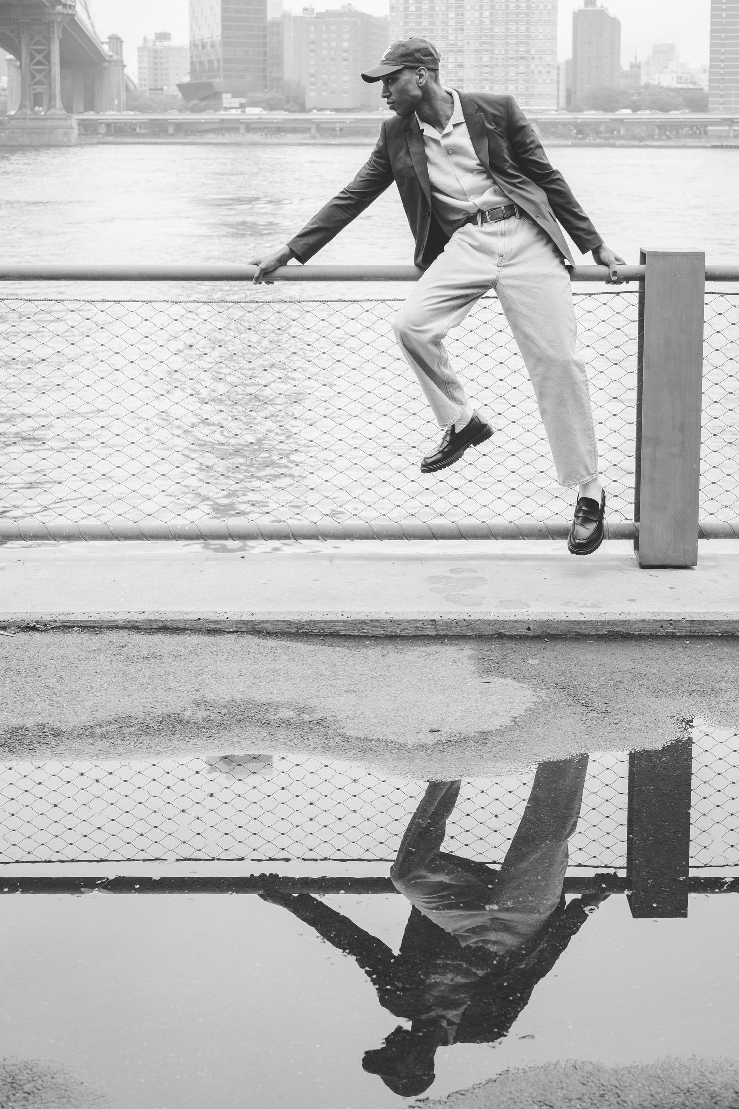 A man sitting on a fence with his reflection in the scene
